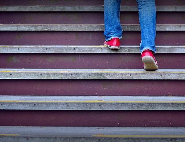 Close-up of person walking upstairs in blue jeans and red shoes.