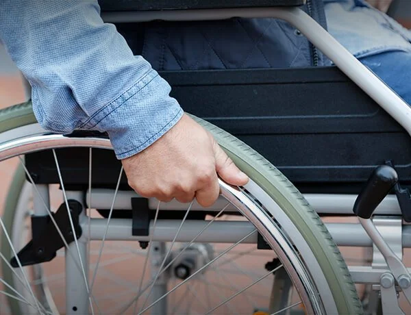 A close-up of a person holding a wheelchair wheel with their left hand, wearing a blue long sleeve shirt.