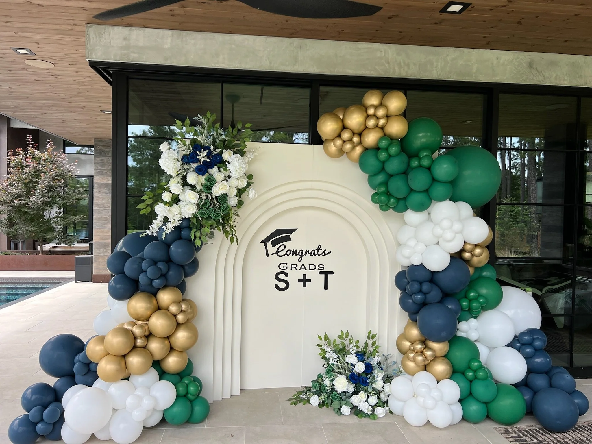 Graduation-themed balloon decoration with floral arrangements and a backdrop that reads 'Congrats Grads S+T'.