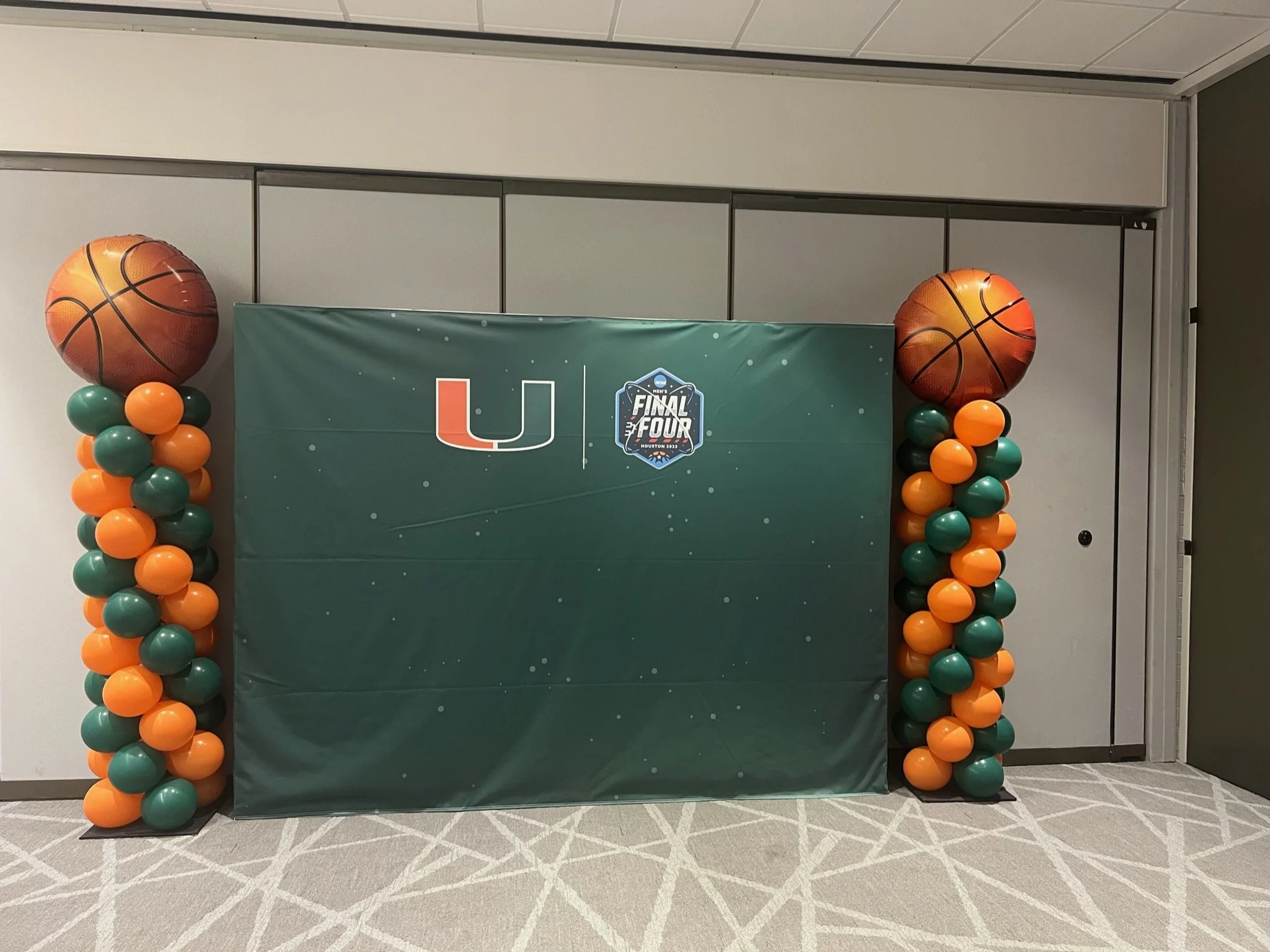 Decorative display for a basketball event featuring two balloon columns with basketball-shaped balloons at the top, surrounding a green backdrop with the University of Miami logo and the Final Four logo.