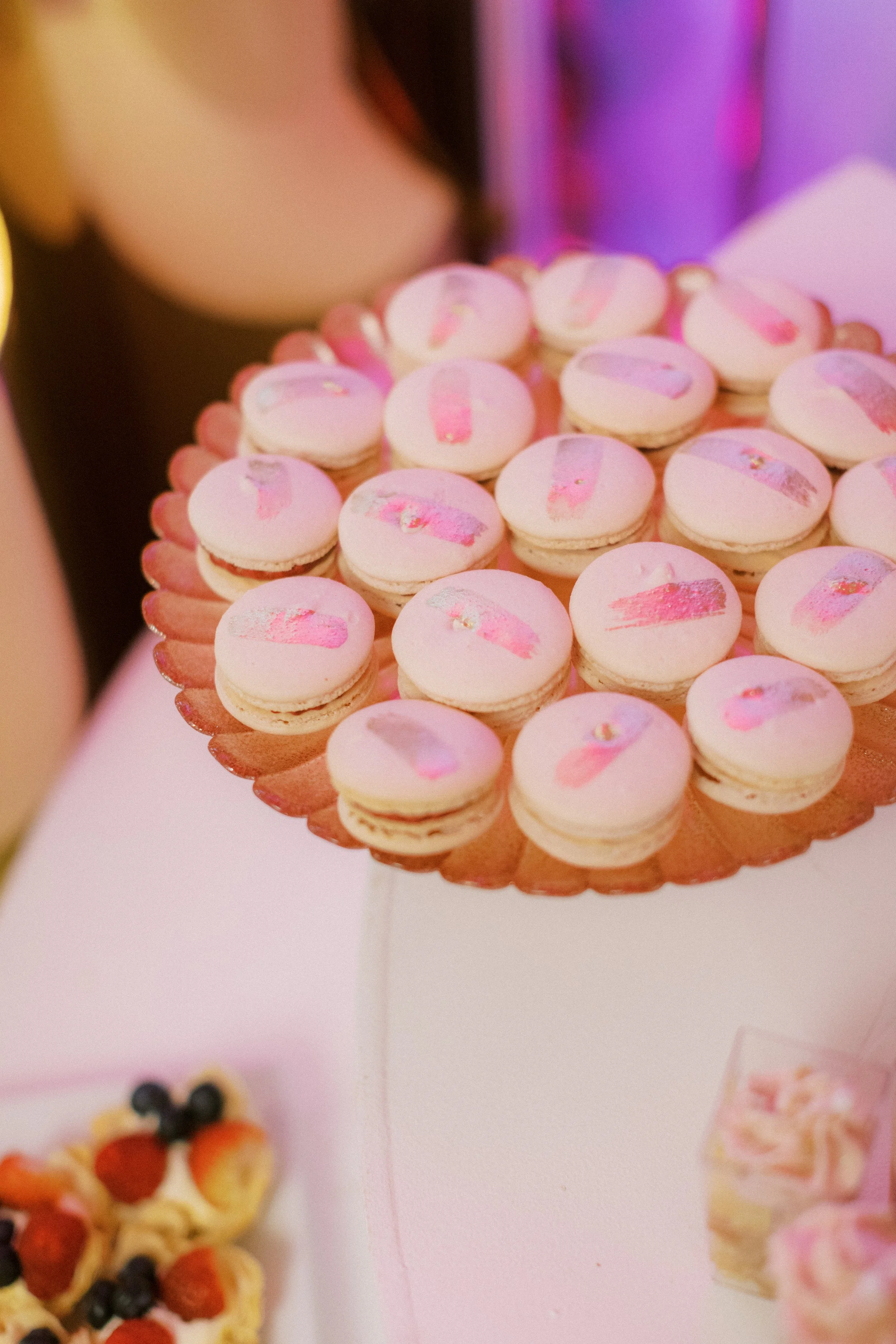 A display of pink macarons on a decorative stand at a celebration or party.