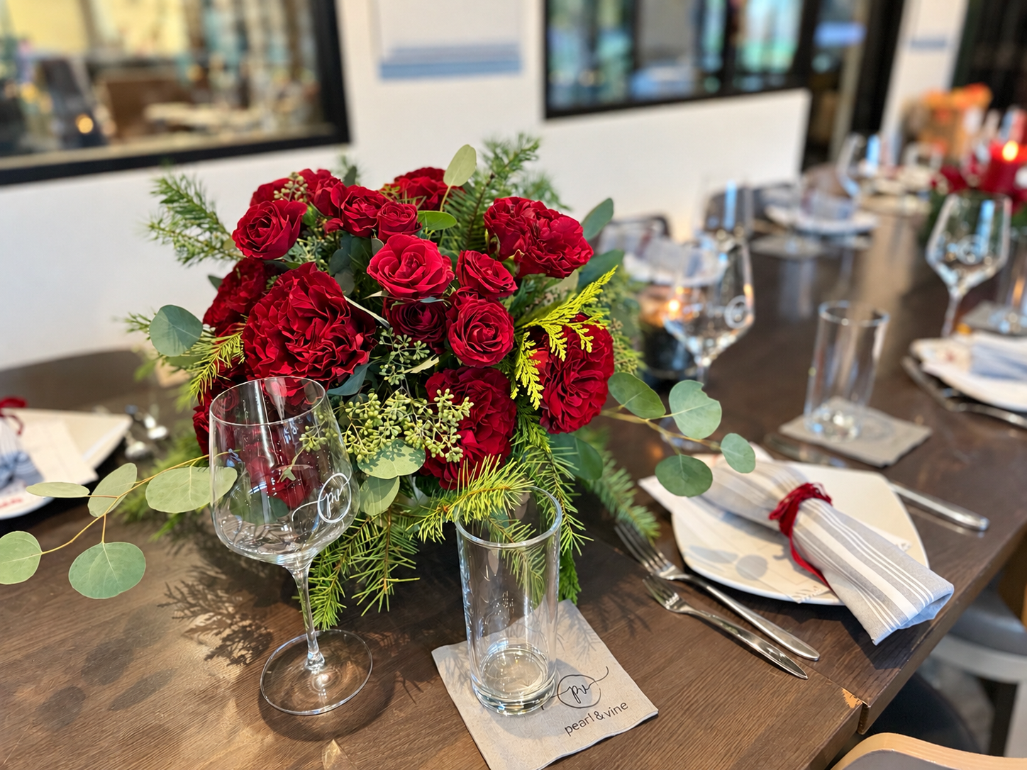 Red rose and carnation centerpiece with eucalyptus and evergreen branches on a holiday dining table.