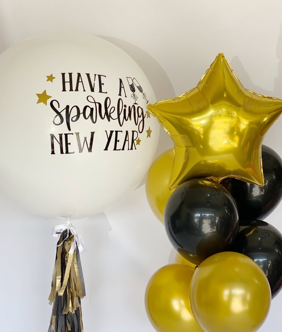 A large white balloon with the message 'Have a sparkling new year' and gold stars, alongside a cluster of gold, black, and metallic balloons, including a gold star-shaped balloon.