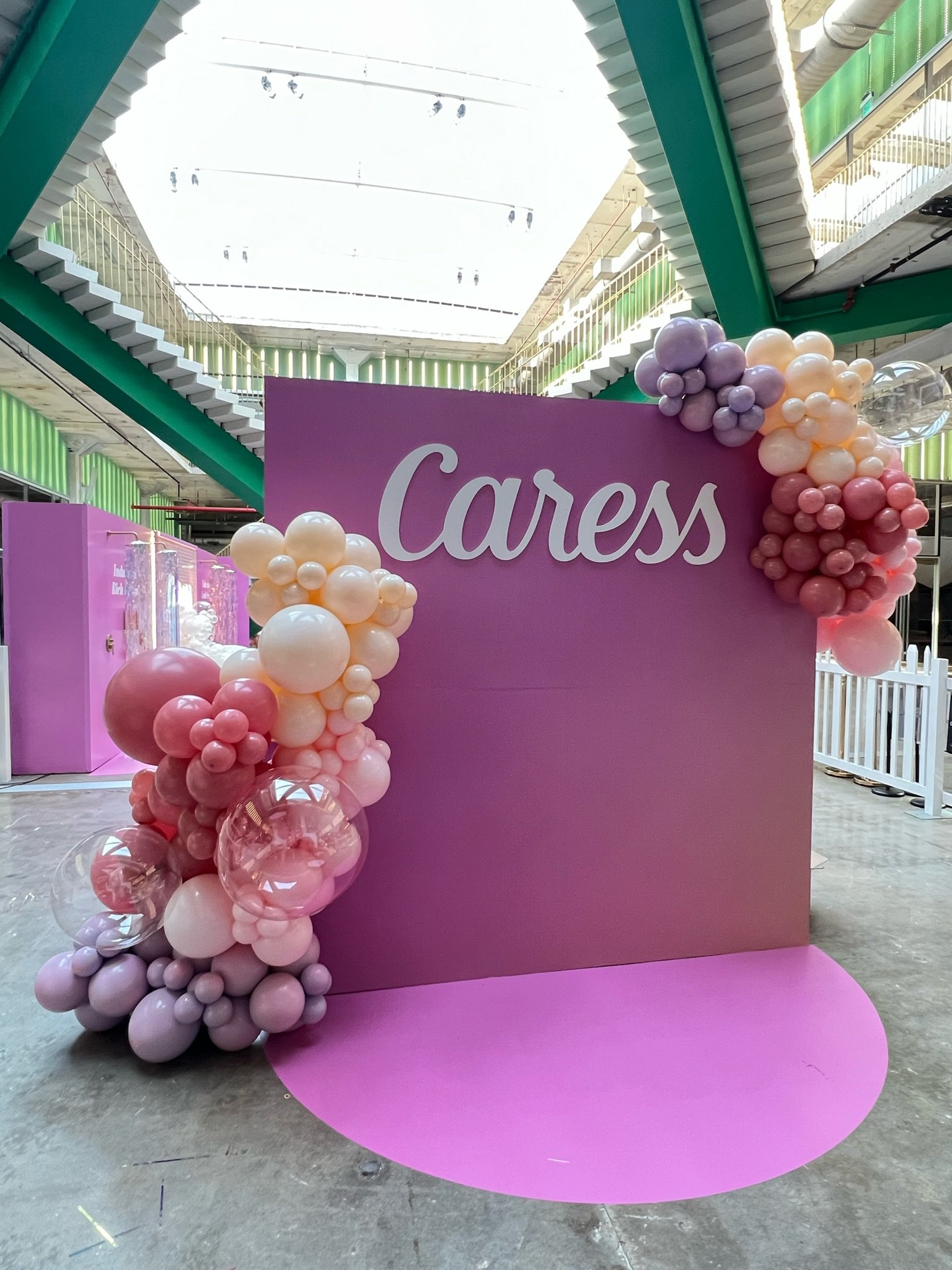 Pink display board with the word 'Cares' written on it, decorated with pastel-colored balloons in pink, peach, purple, and clear, arranged on the left and top right corners.