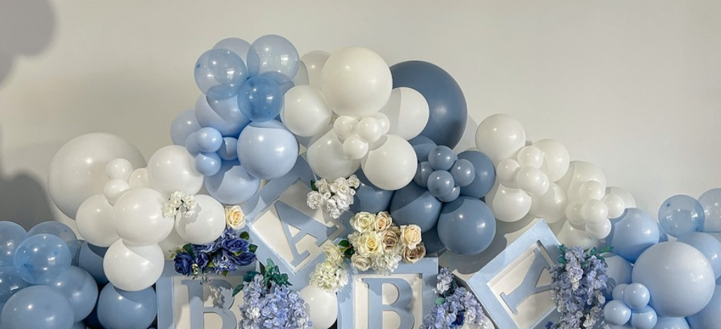 Decorative balloon arrangement in shades of white and blue with floral accents and letter blocks.
