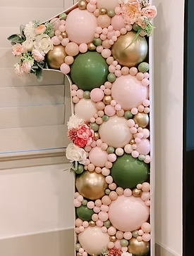 Vertical balloon display with pink, green, and gold balloons accompanied by flowers.