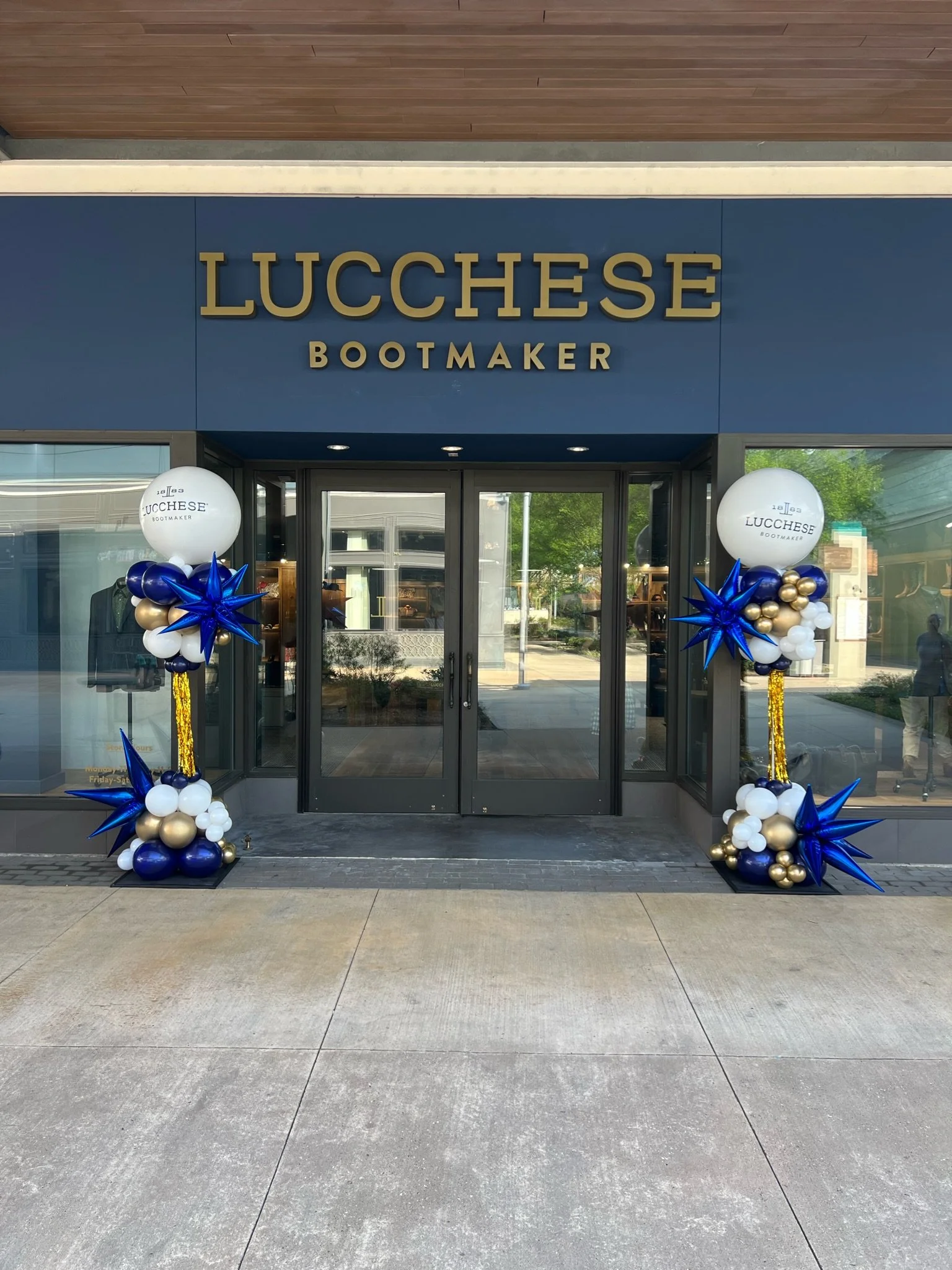 Storefront of Lucchese Bootmaker with blue, white, and gold balloon decorations on either side of the entrance.
