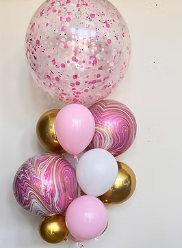 A cluster of twelve balloons, including a large confetti-filled balloon, marbled pink and gold balloons, plain pink, white, and gold balloons arranged against a plain wall.
