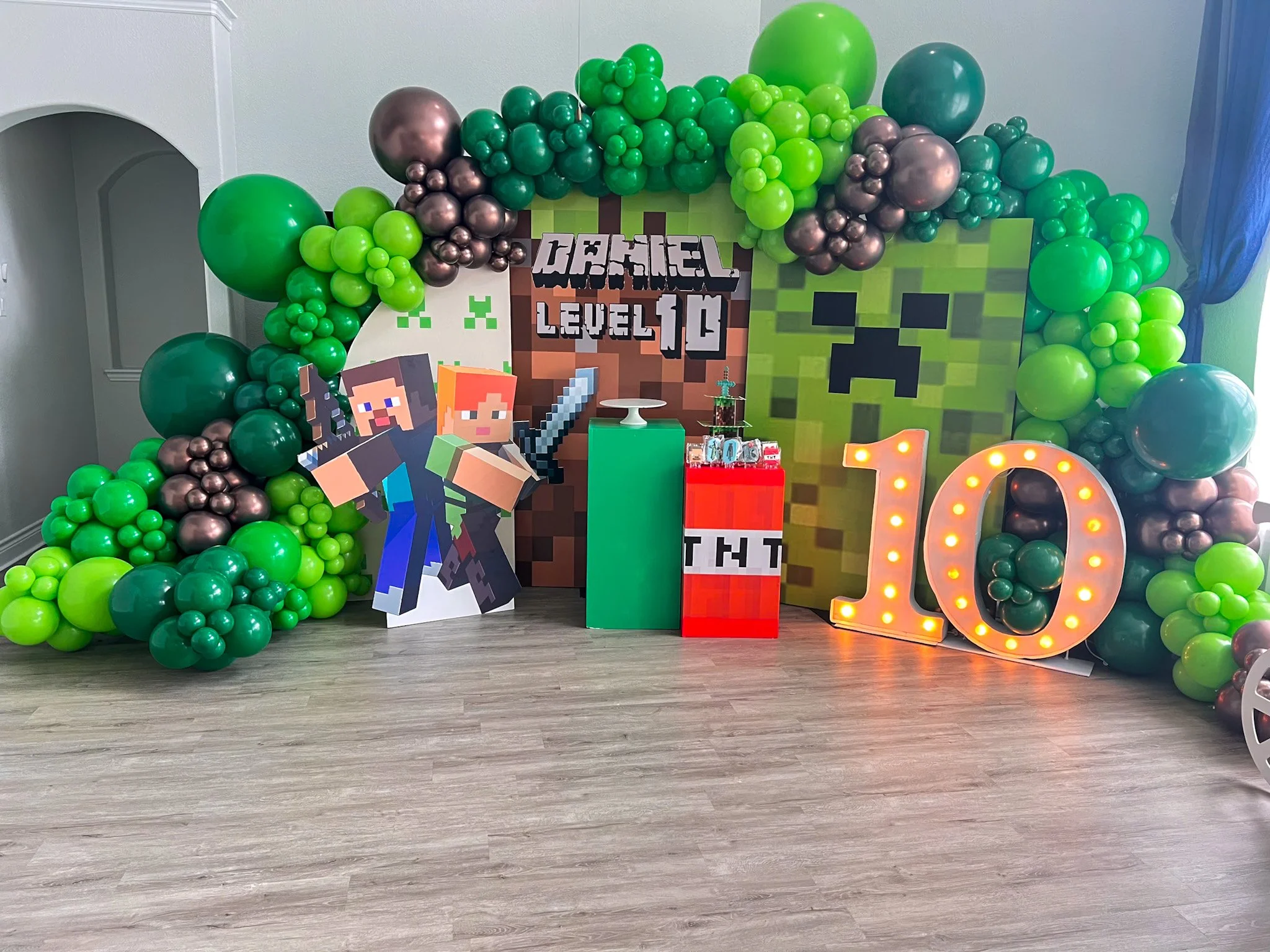 Minecraft-themed birthday party decorations with green and brown balloons, pixel art characters, a large number 10 sign with lights, and Minecraft-themed backgrounds.