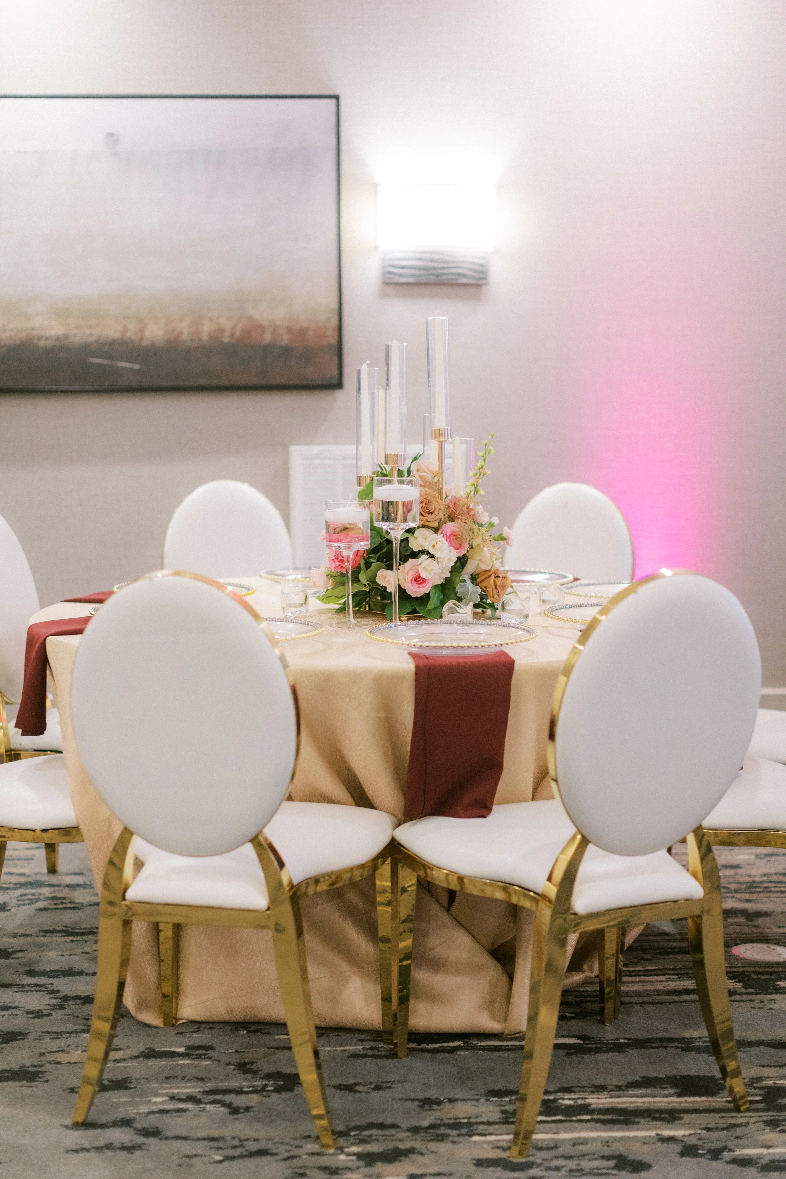Round banquet table decorated with a flower centerpiece, surrounded by six white chairs with gold trim, set for a formal event.