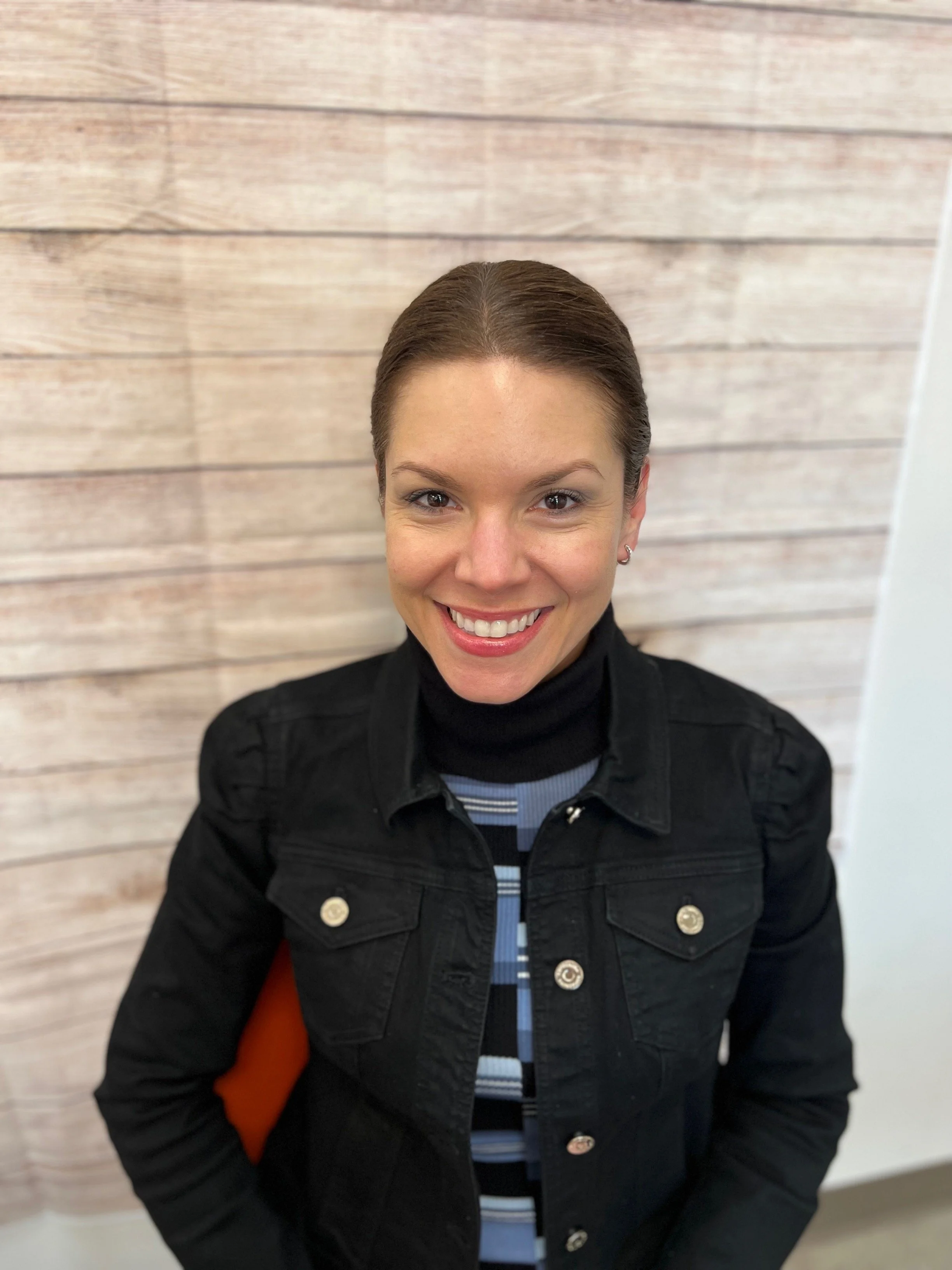 Board member with hair pulled back smiling in portrait against light wood wall, Cocoon House Snohomish County