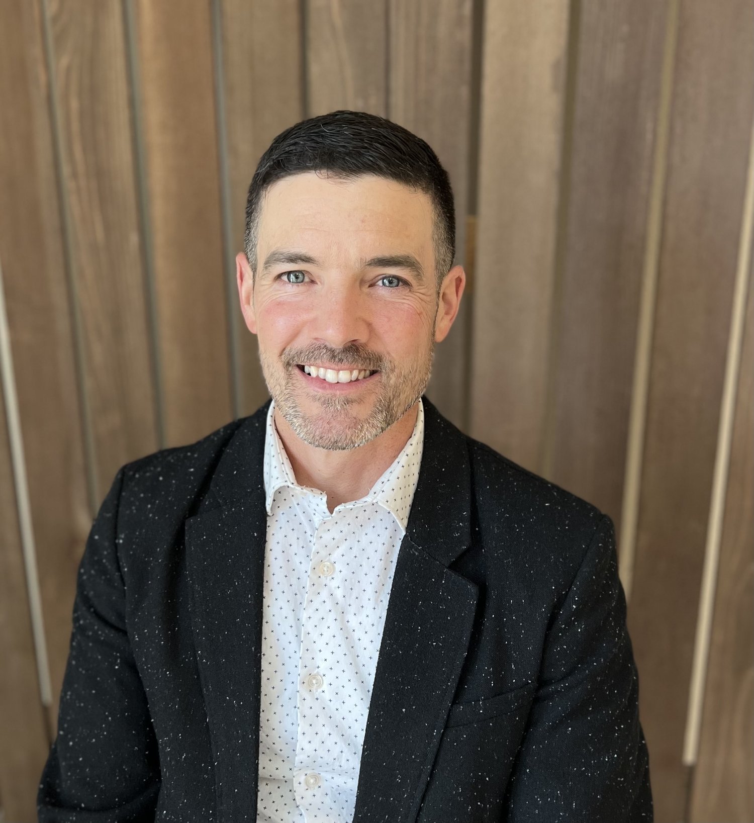 Joseph Alonzo smiling in professional portrait against wooden backdrop, representing Cocoon House leadership in Snohomish County