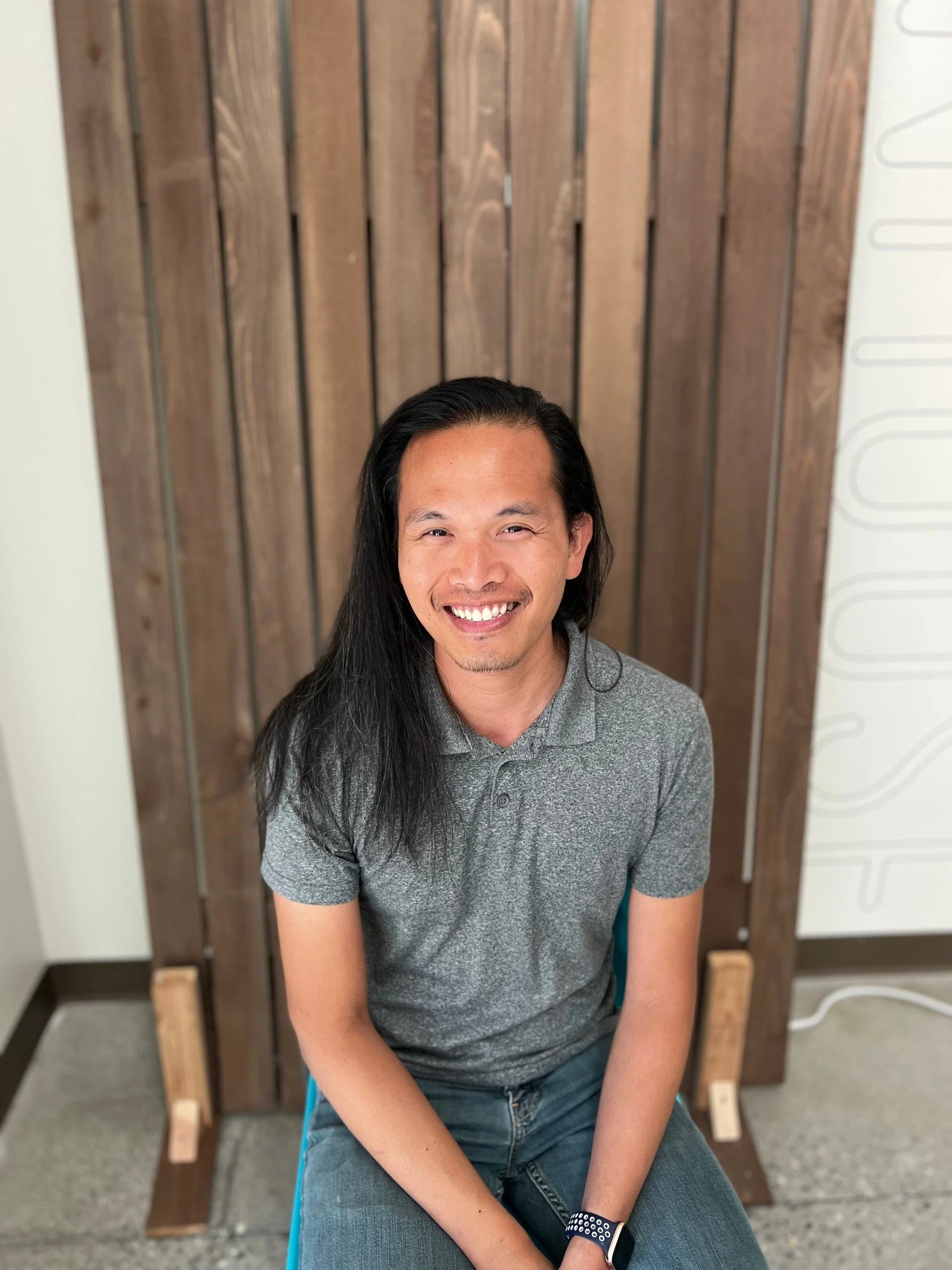 Board member with long hair smiling in seated portrait against wooden background, Cocoon House Snohomish County