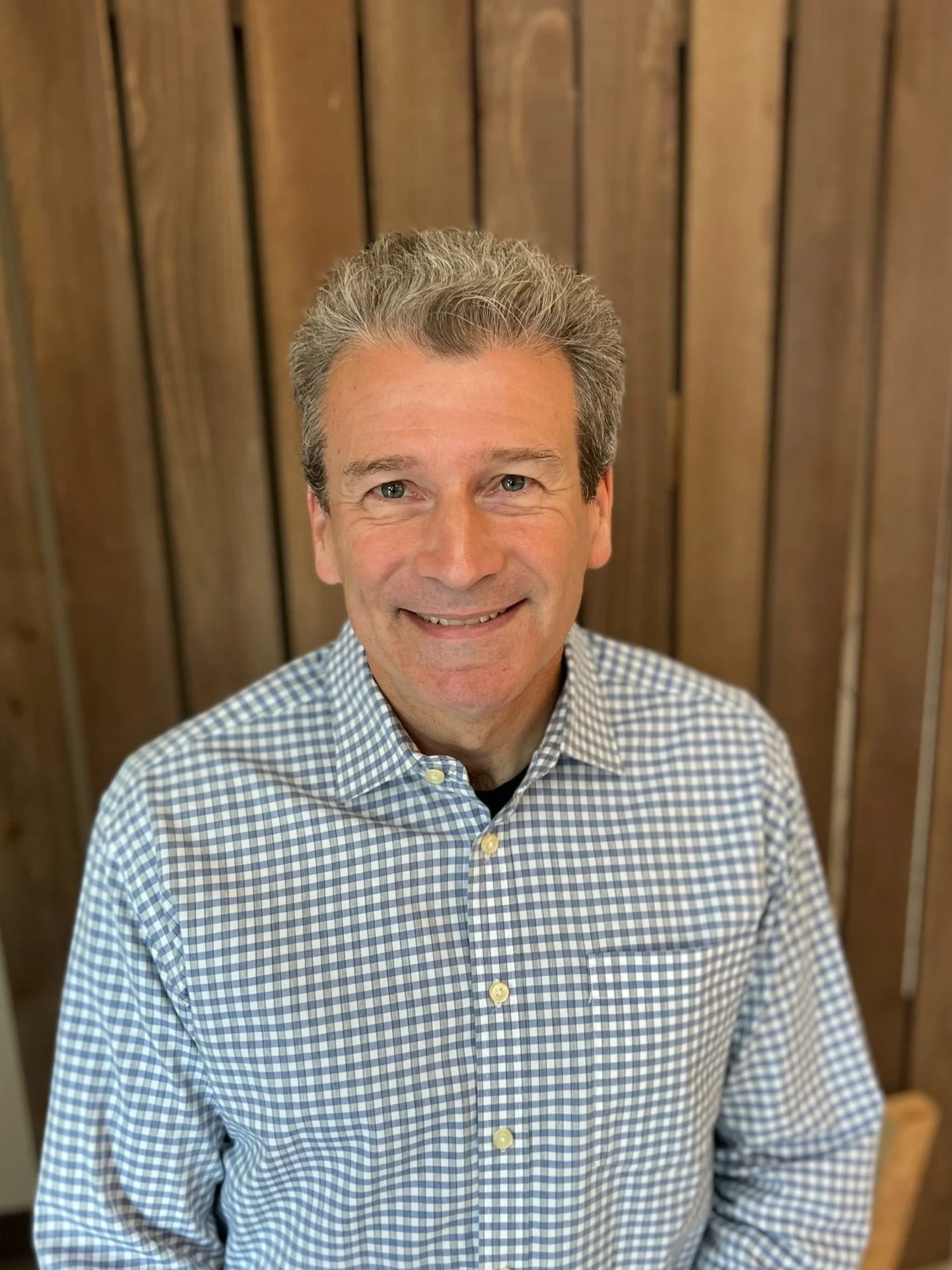 Chris Willis smiling in professional portrait against wooden backdrop, representing Cocoon House leadership in Snohomish County