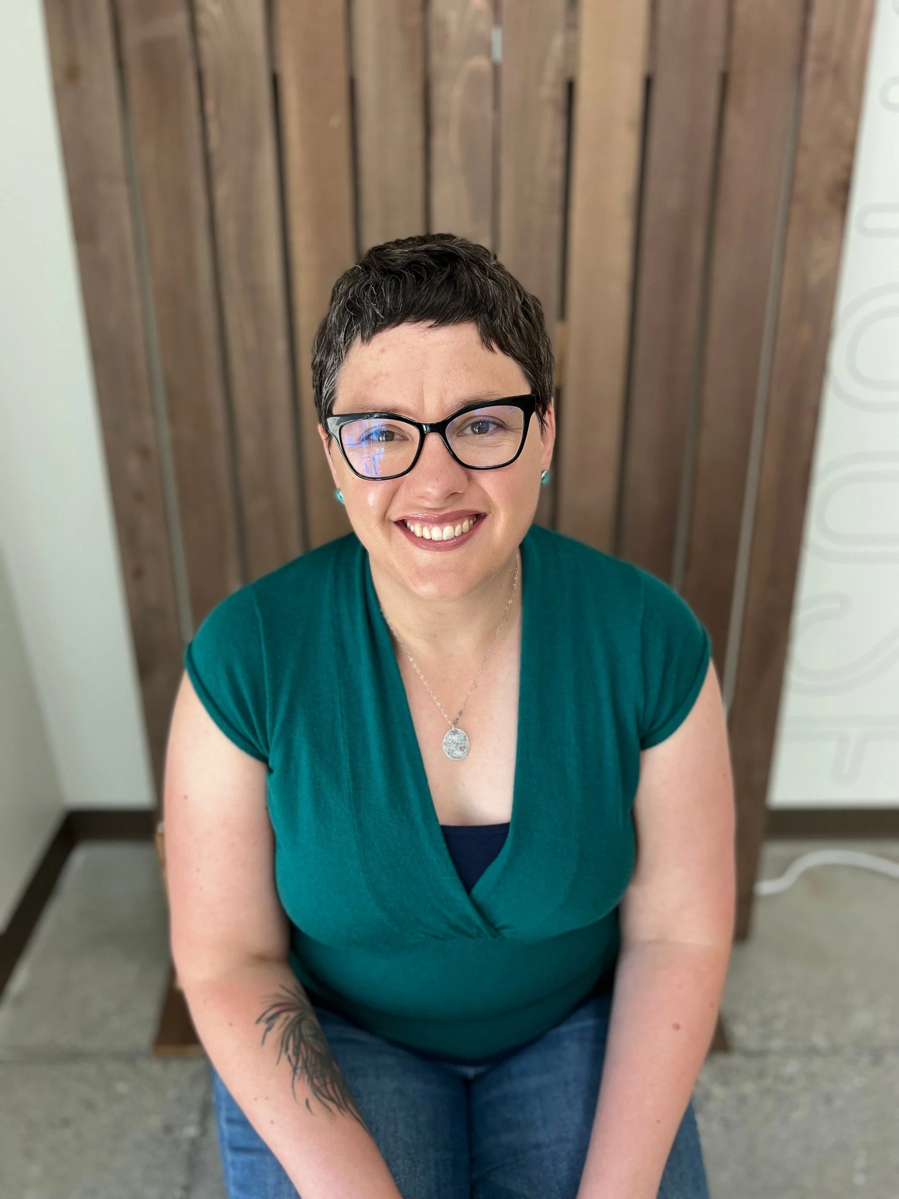 Board member with glasses smiling in seated portrait against wooden background, Cocoon House Snohomish County