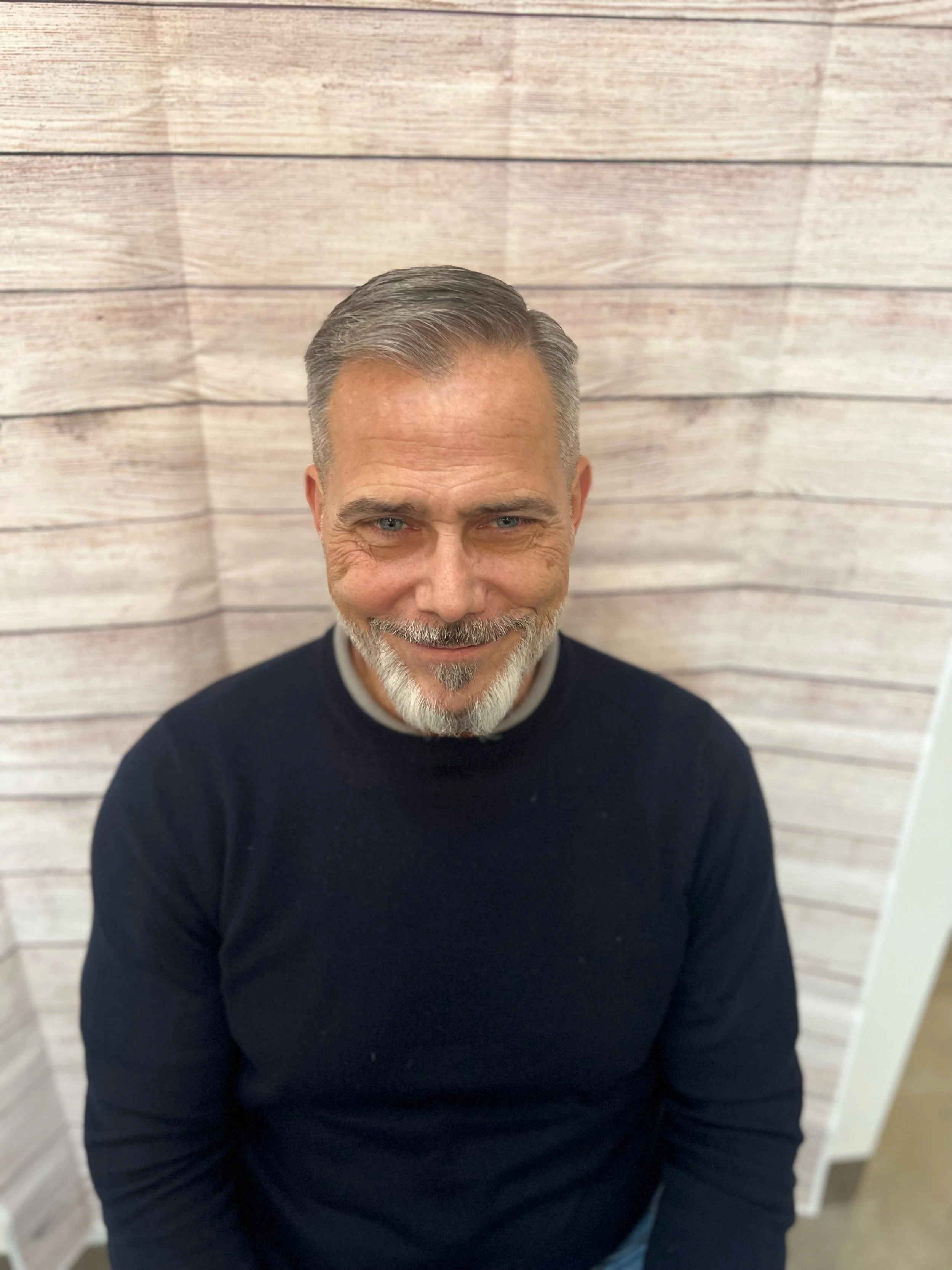Board member with gray hair and beard smiling in seated portrait against wooden background, Cocoon House Snohomish County