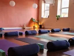 Yoga mats, blankets, and cushions in a brightly lit yoga studio with pink walls and windows.