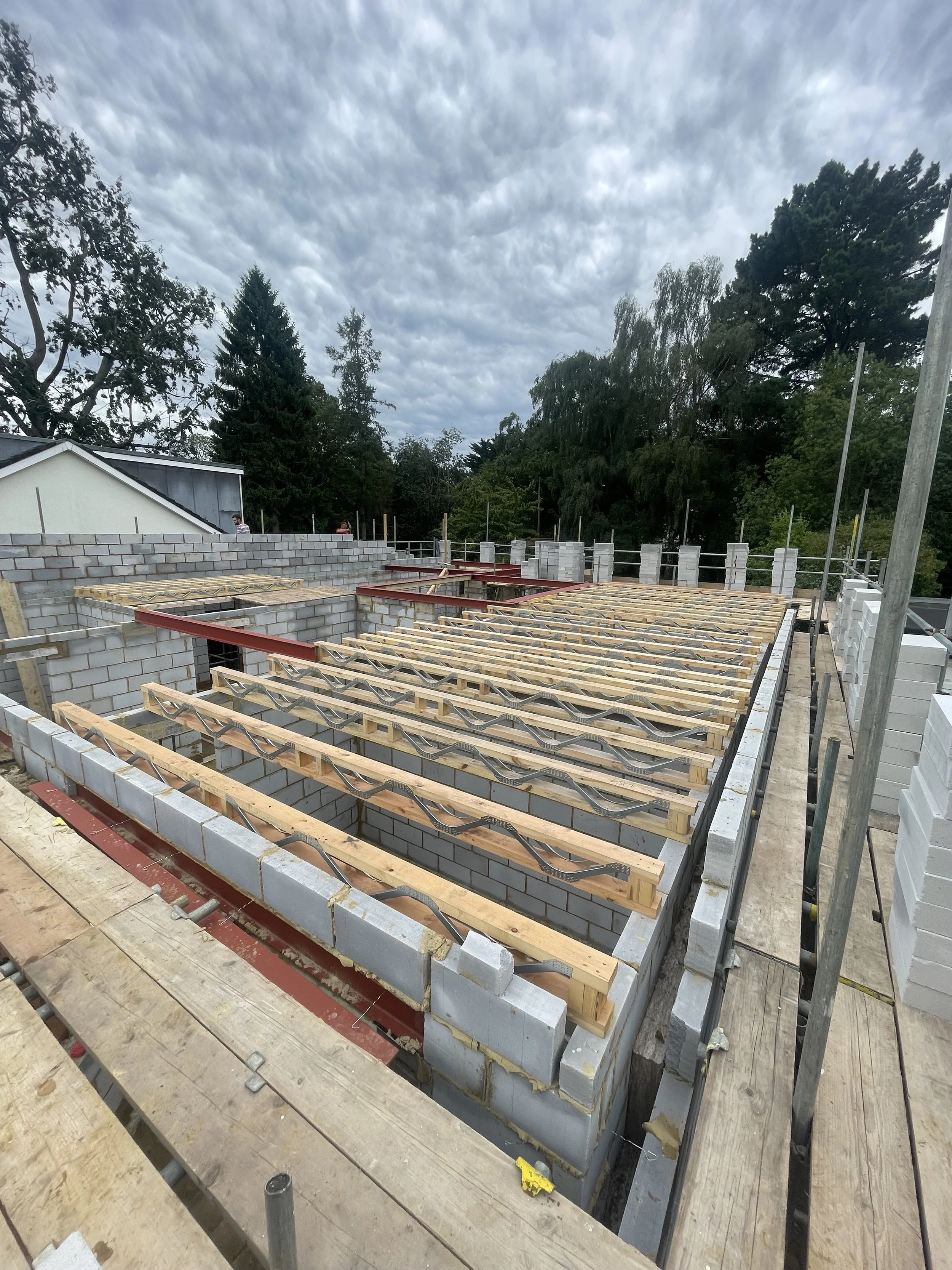 Construction site with brick walls and wooden framework for a building roof, under cloudy sky.
