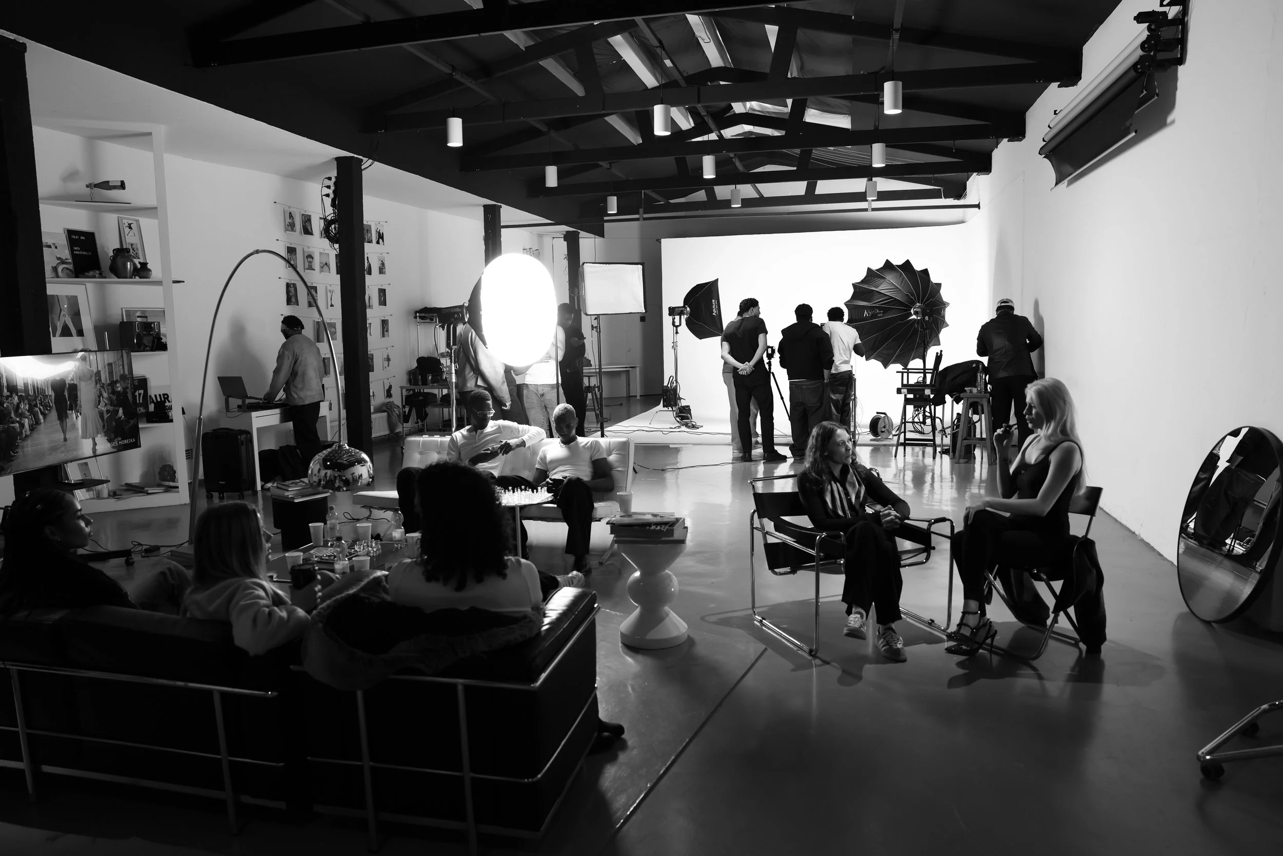 Blick in ein Fotostudio mit mehreren Menschen, Beleuchtung, Kameraausrüstung und einem weißen Hintergrund, Szene für ein Fotoshooting.