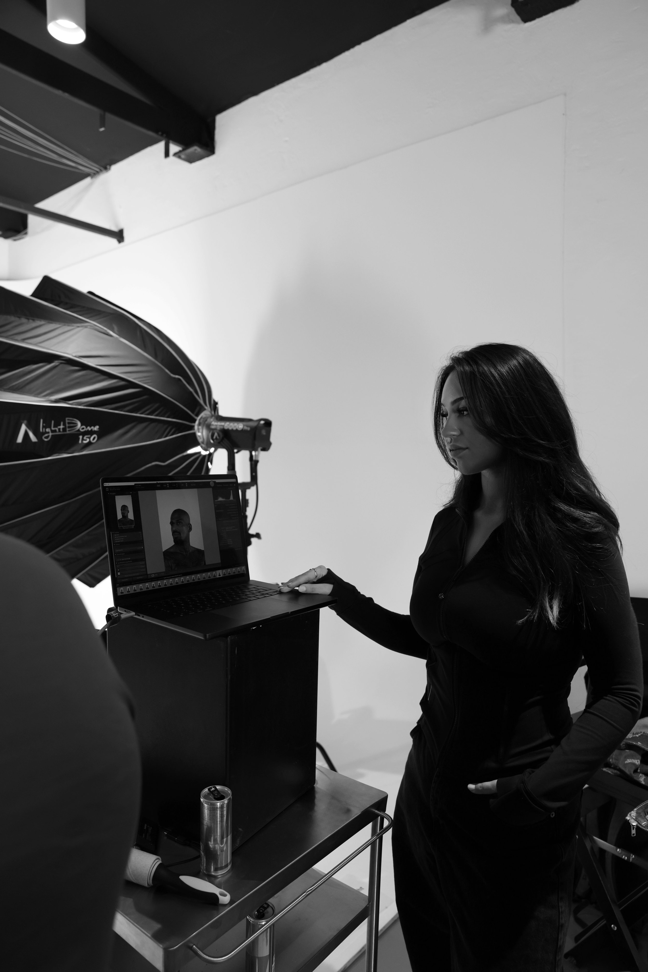 Frau bei Fotoshooting im Fotostudio, schwarz-weiß, mit Studioausrüstung und Fotograf-Computer.