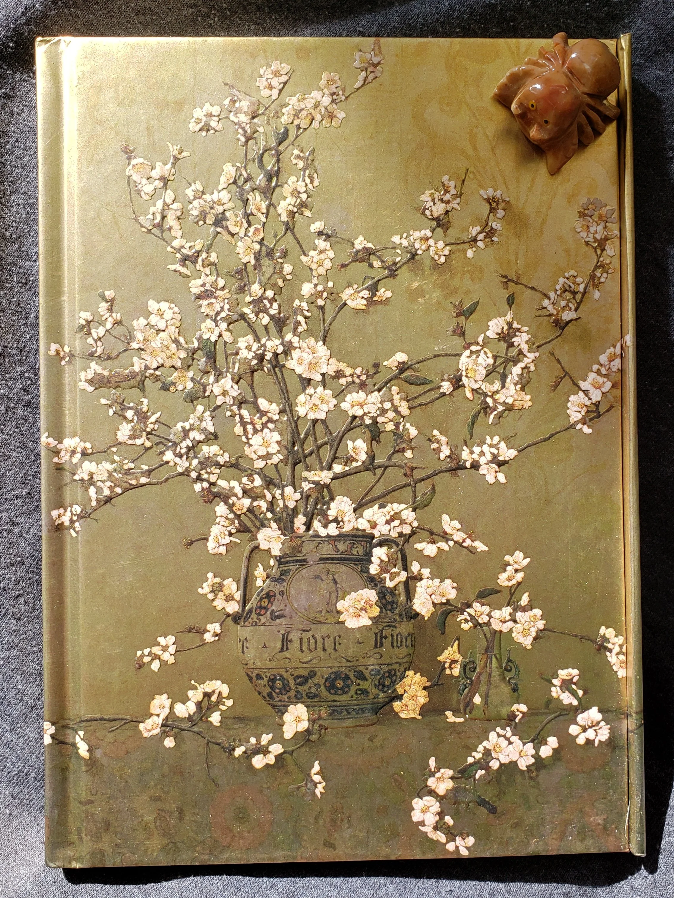 Gold journal with a vase and apple blossoms and branches on the cover.