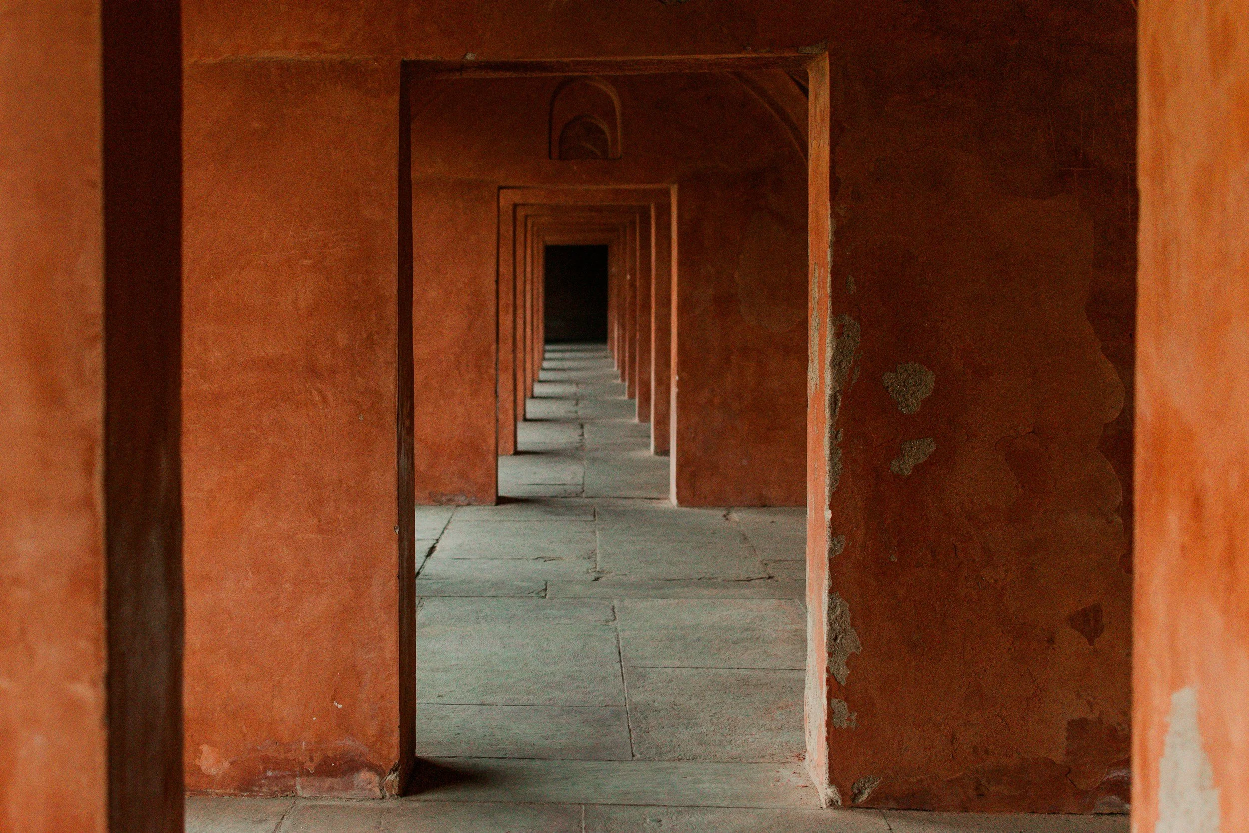 Series of arches and doorways in red sandstone, leading into a corridor with gray stone paving.