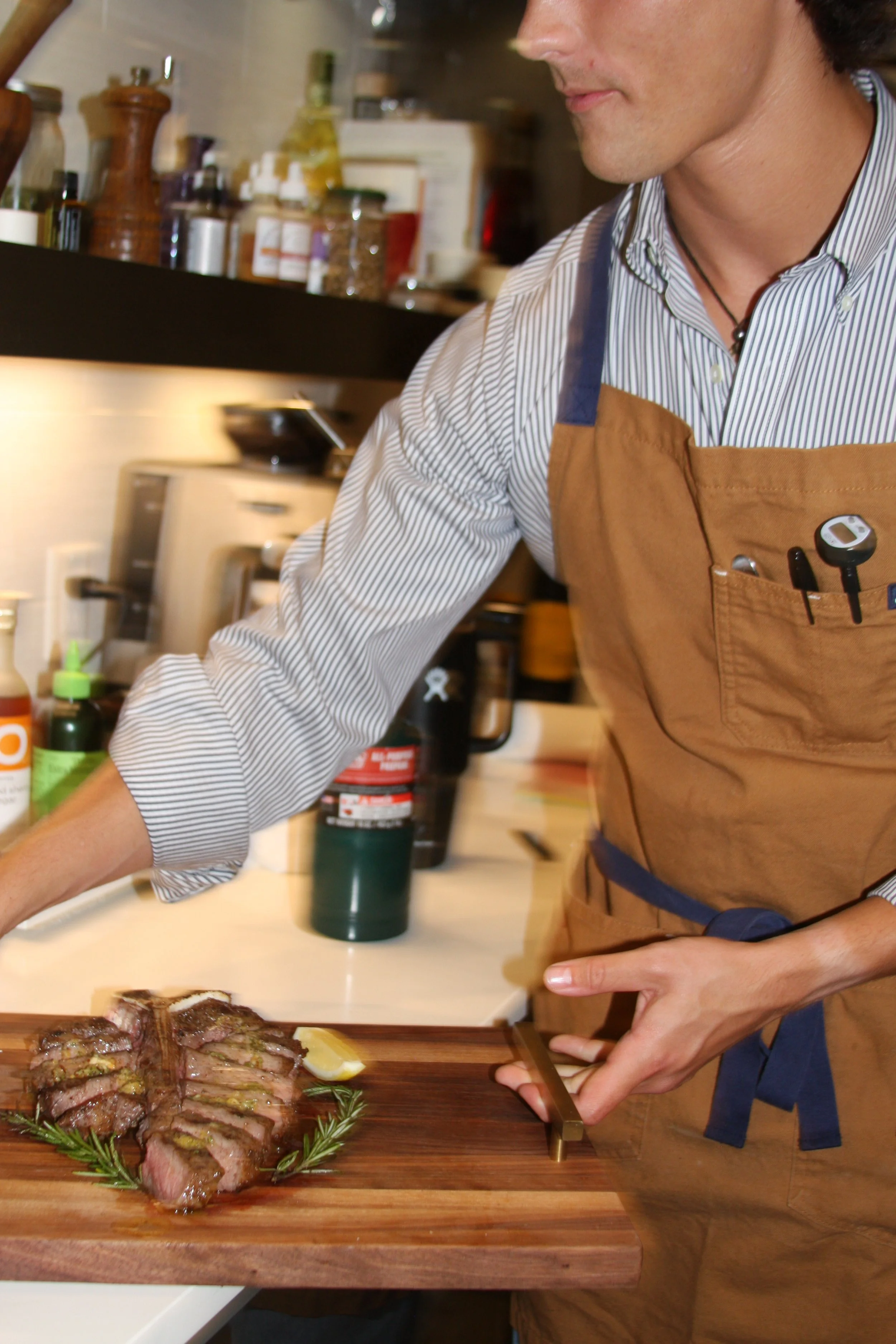 Person slicing cooked steak on a wooden cutting board in a kitchen.
