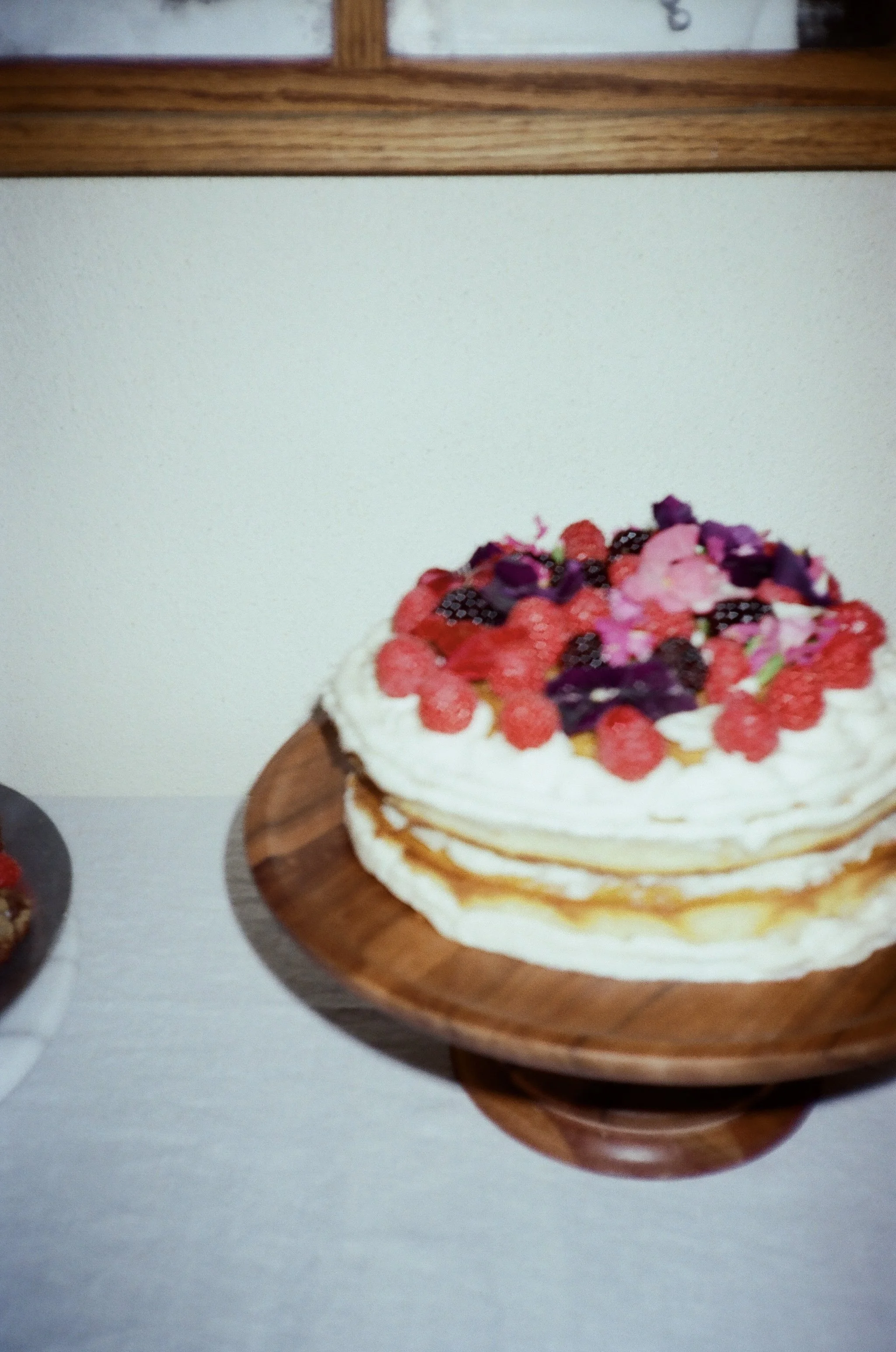 A layered cake topped with fresh berries and edible flowers on a wooden plate.