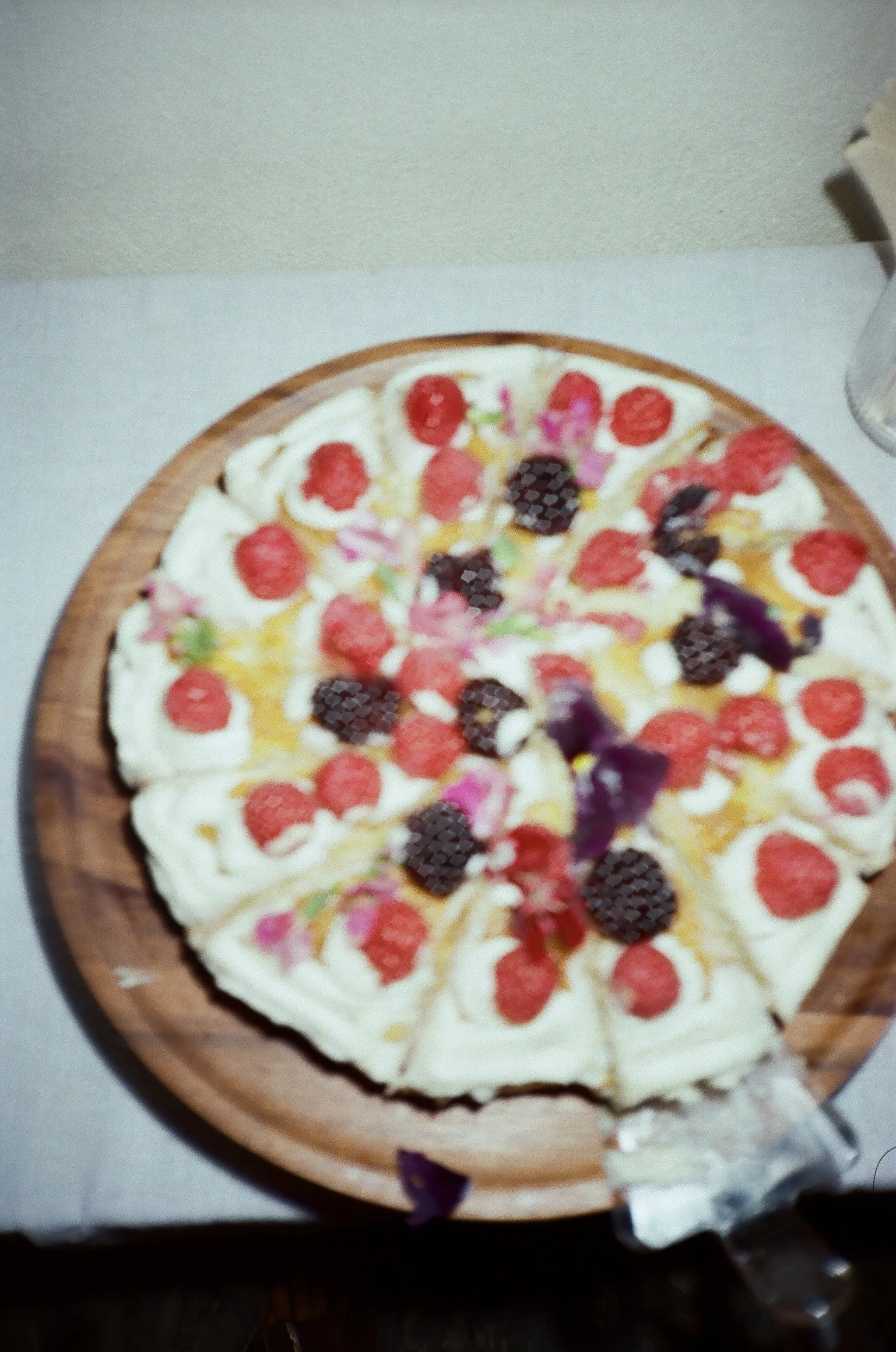 A fruit pizza with whipped cream and assorted berries on a wooden serving tray.