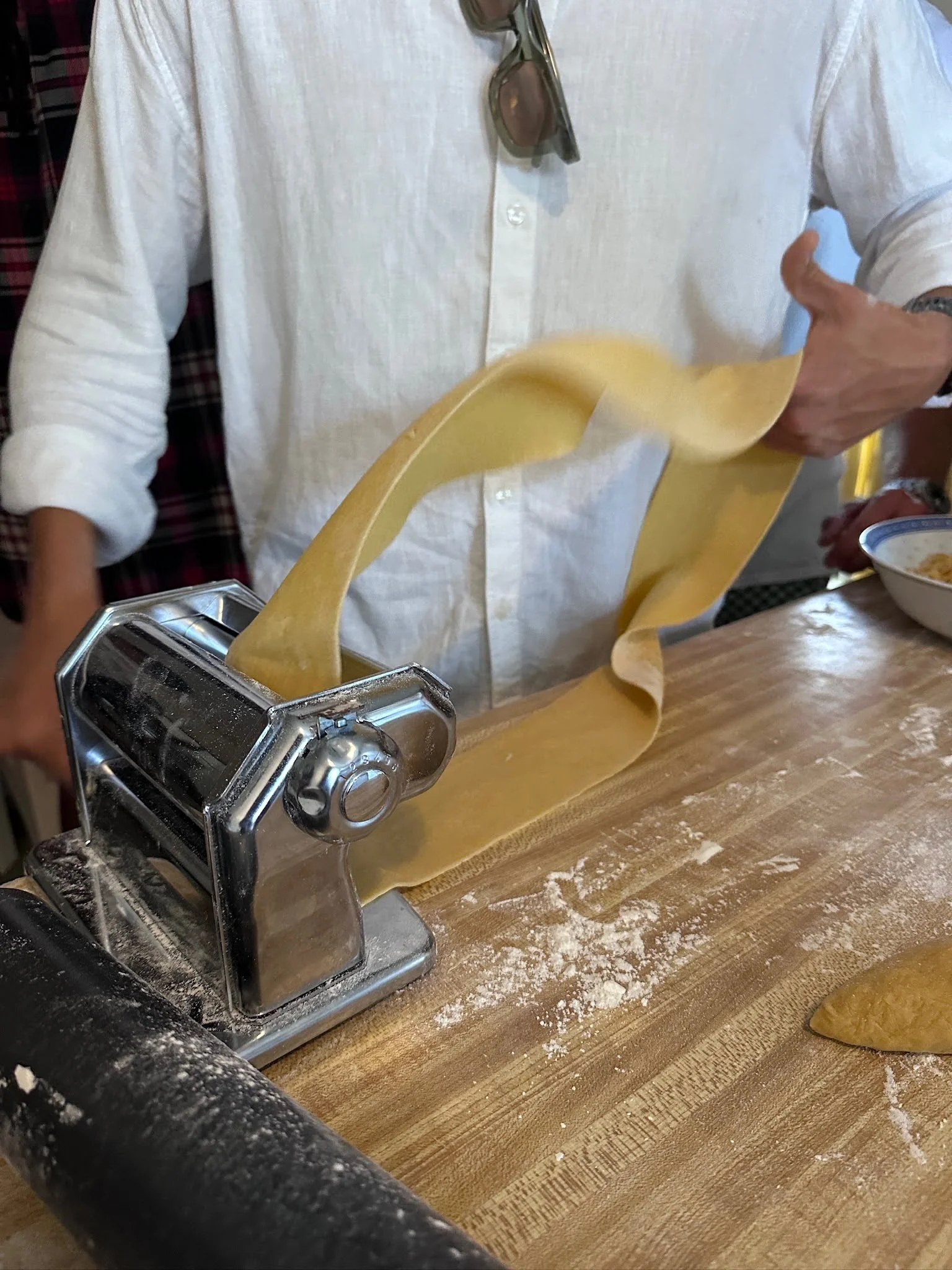 Person rolling out pasta dough with a pasta machine on a wooden countertop