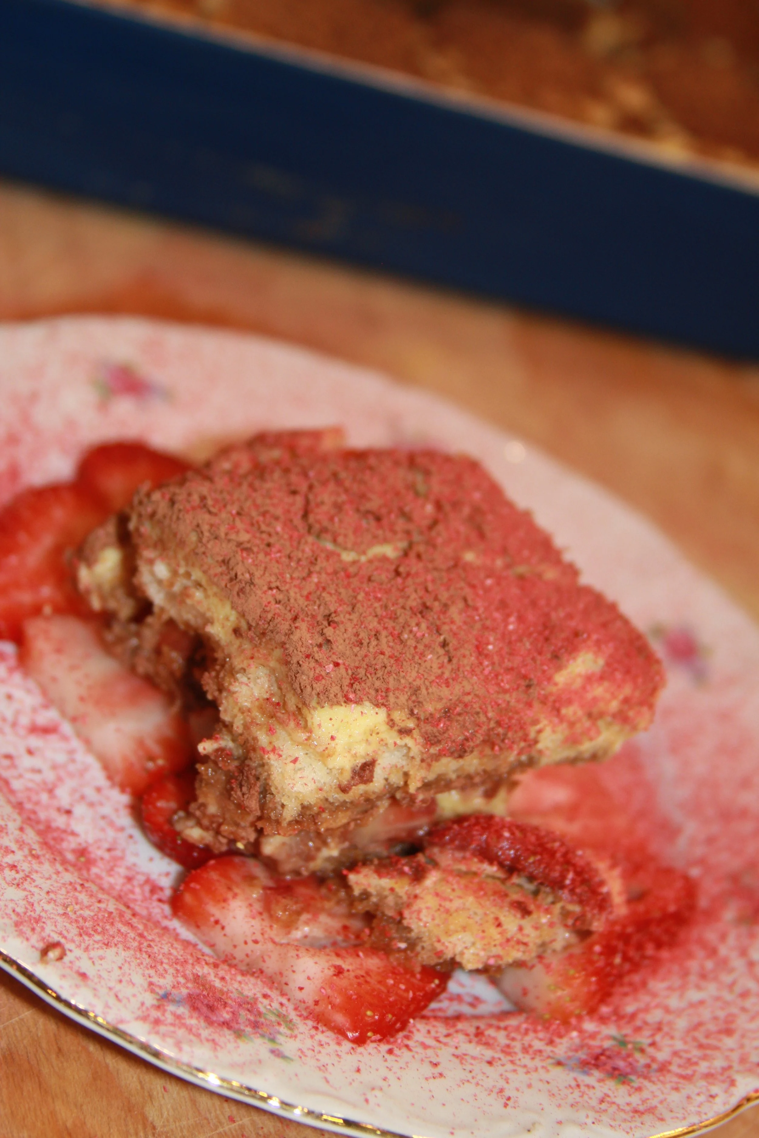 A partially eaten strawberry blind dessert on a decorative plate with red powder and strawberry slices.