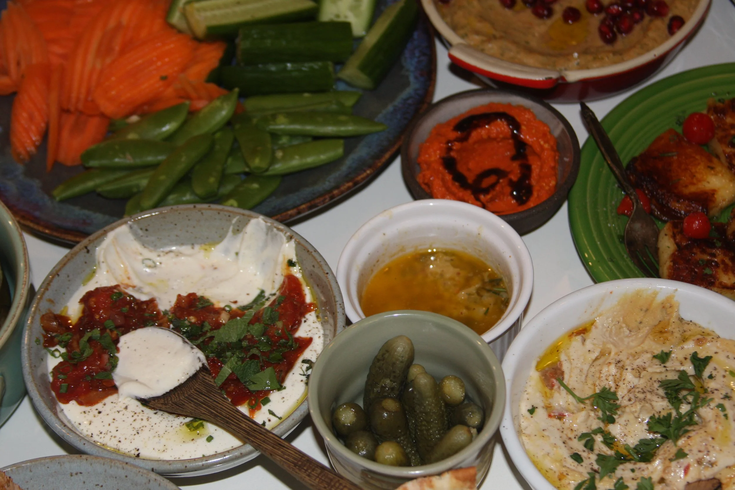 A variety of Middle Eastern dishes including fresh vegetables, dips, pickles, and grilled meats on colorful plates.