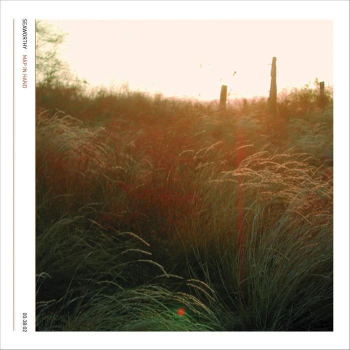 Sunset over tall grasses and a fence with wooden posts in a field.