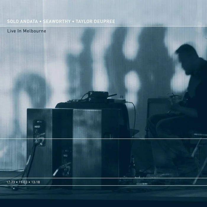 Silhouette of a person sitting next to electronic equipment on stage during a live performance in Melbourne, with a blurred background and shadows.