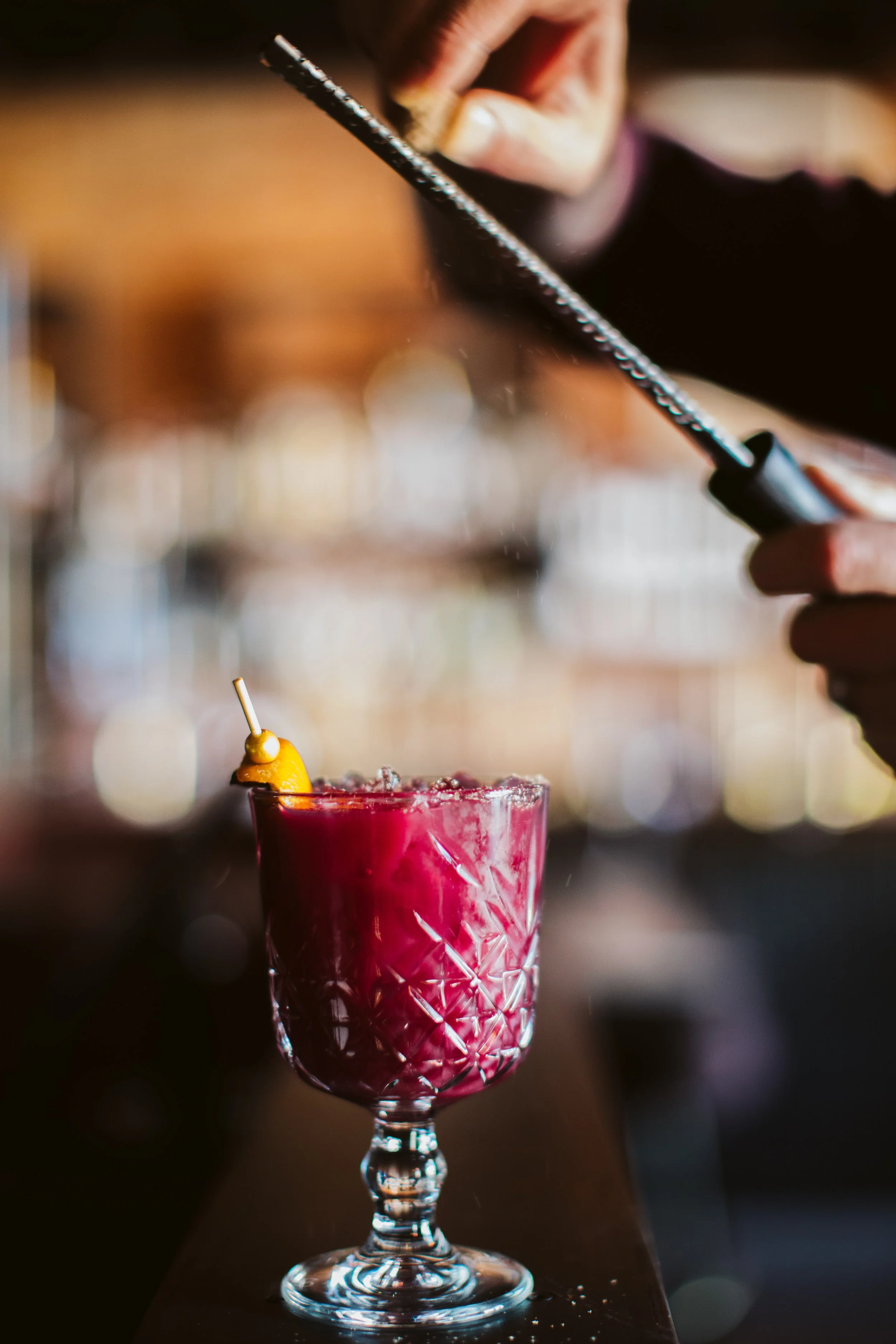 Craft cocktail being garnished with flame at bar