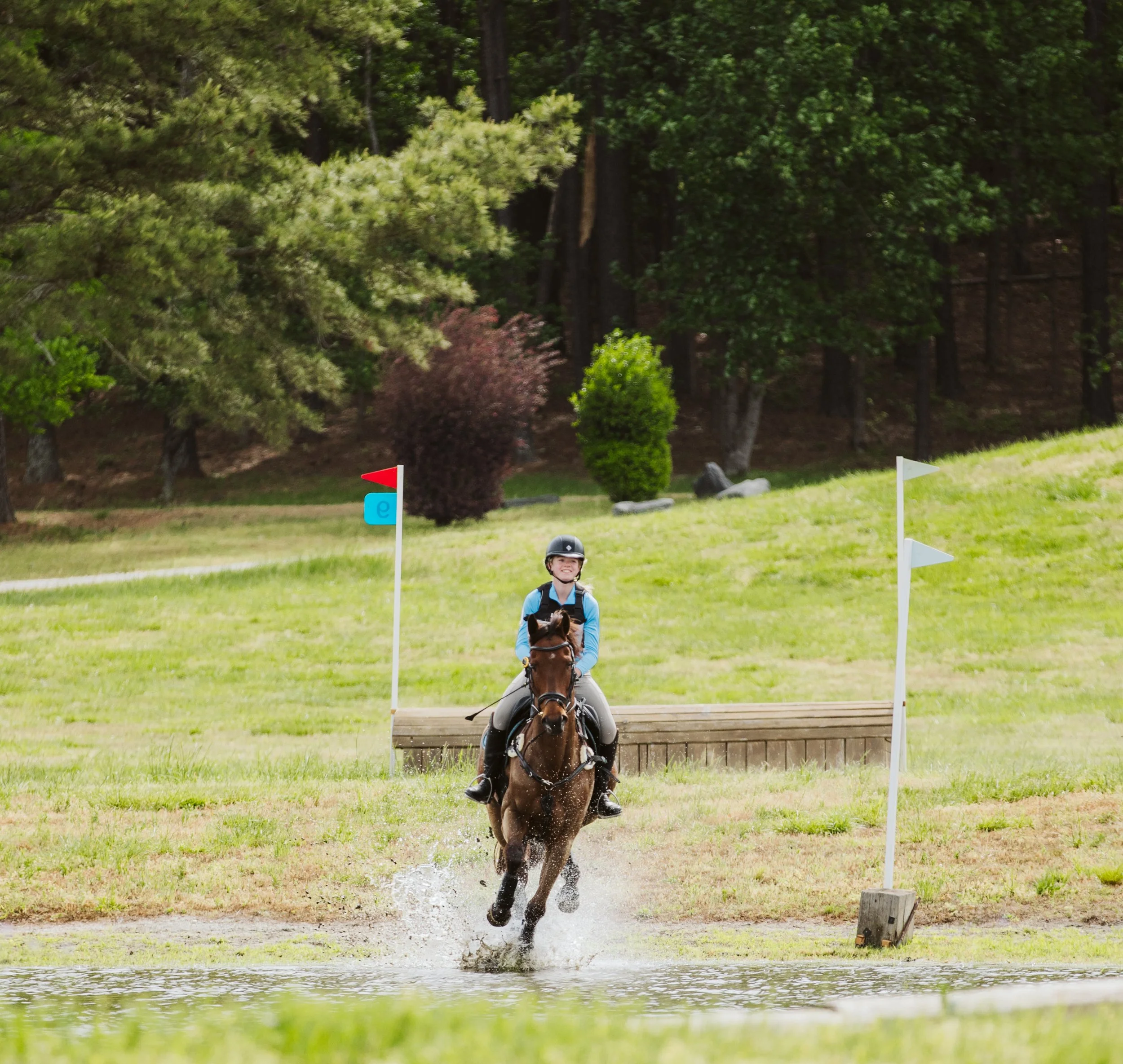 Horse and rider splashing through water obstacle