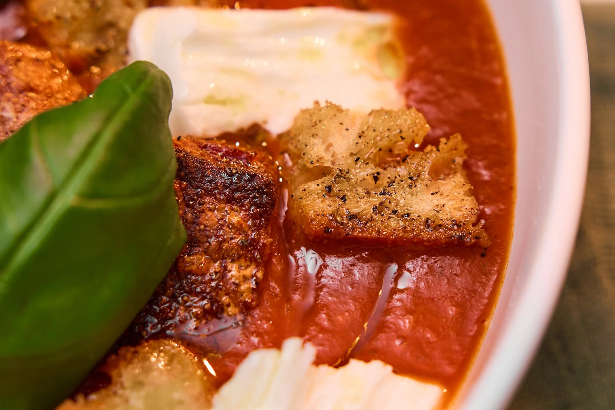 Tomatsuppe med hjemmelaget krutonger med mozarella og basilikum som blir rørt sammen i en gryte.