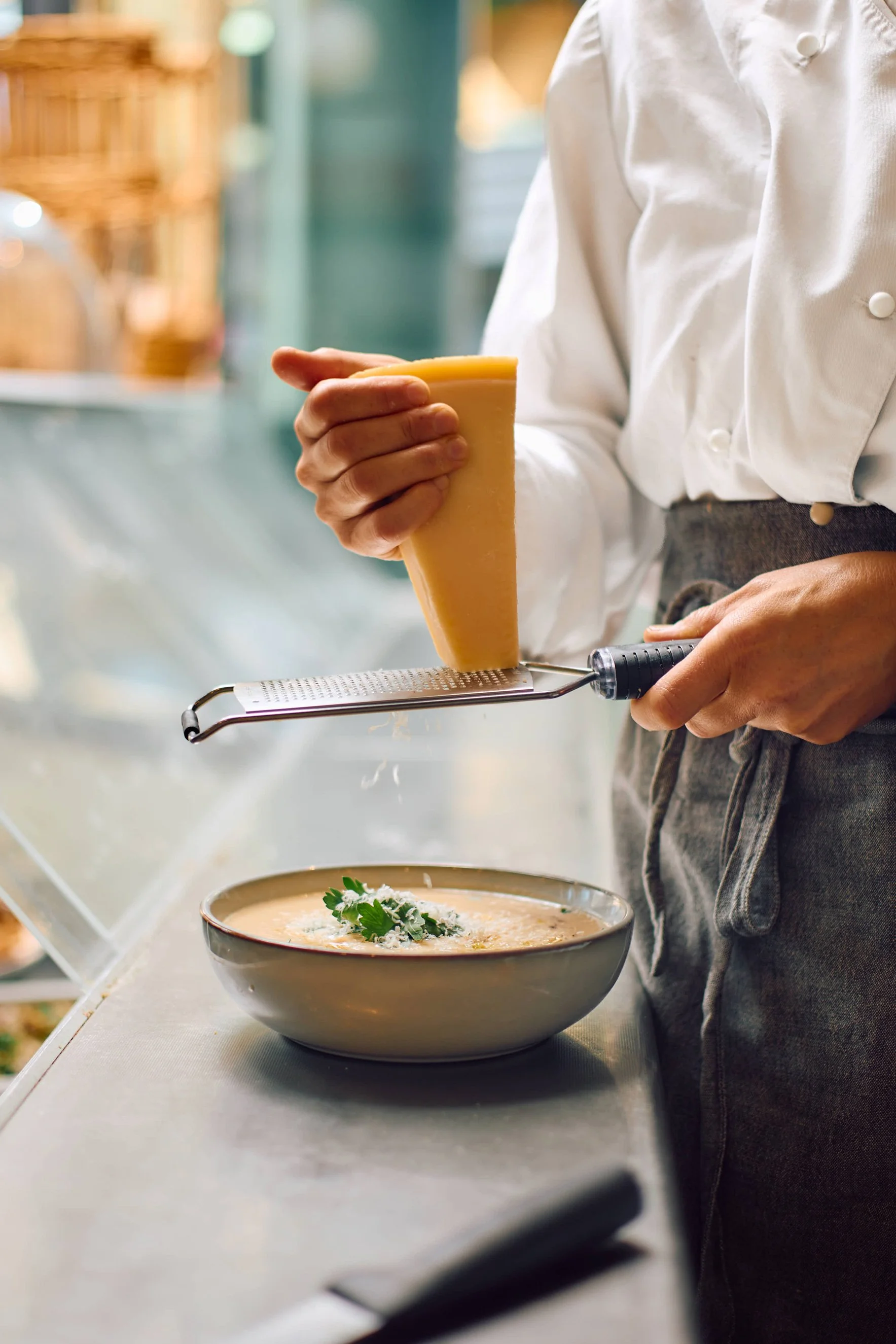 Kokk i uniform står i kantinen og river parmesan over en skål med Foodyfly suppe