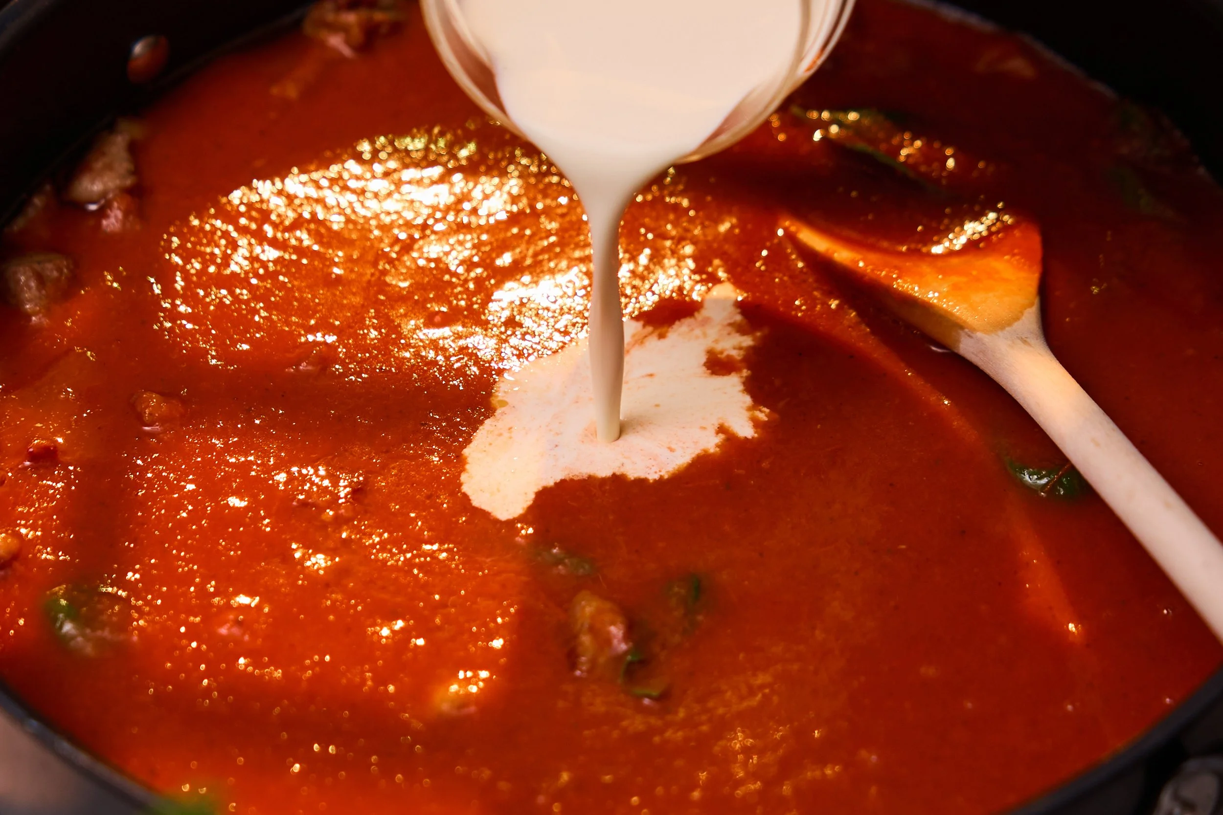 Tomatsuppe  som blir brukt til å lage saus i en gryte, med fløte som helles ned i suppen