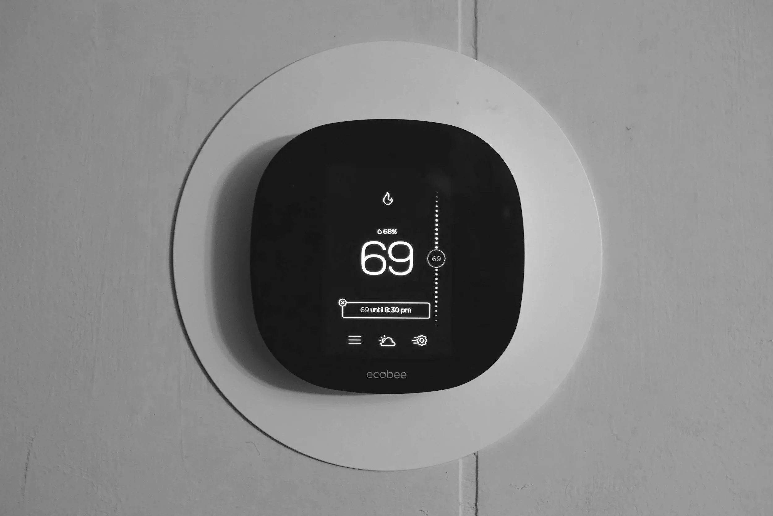 Smart thermostat mounted on a wall showing a temperature of 69°F, humidity level at 68%, and weather icons.