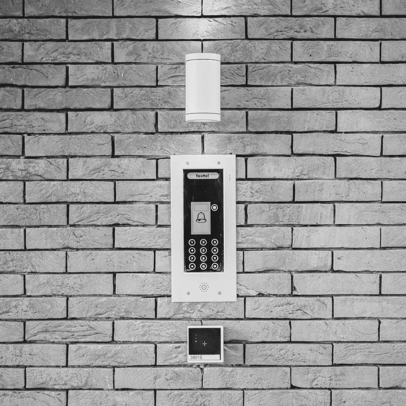 A brick wall with an intercom system featuring a keypad, a bell icon, and a small display screen.
