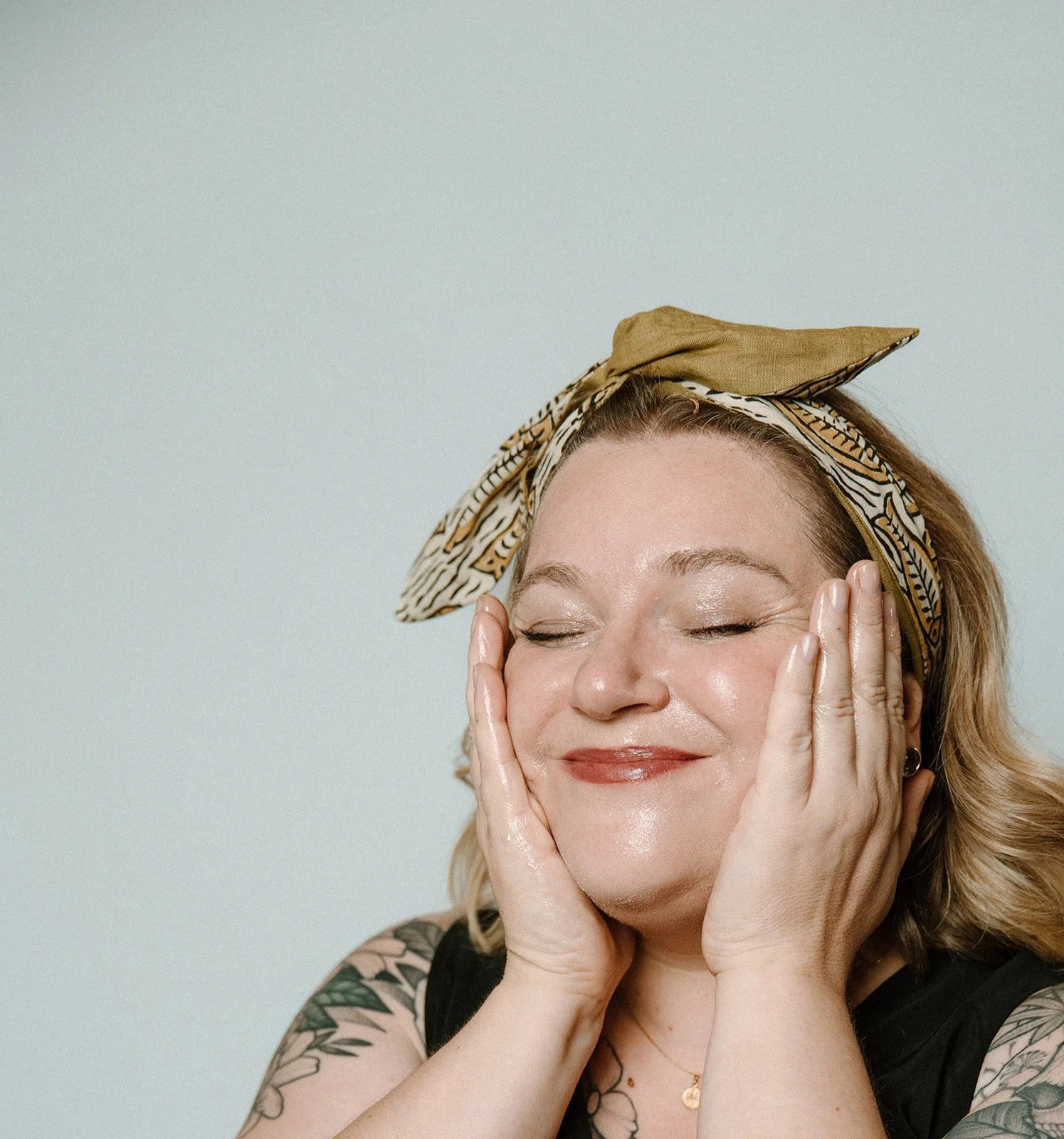 Stephanie is mid-cleanse, with her hair pulled back in a headband. Her hands are on the sides of her face, and the makeup is starting to melt away,.