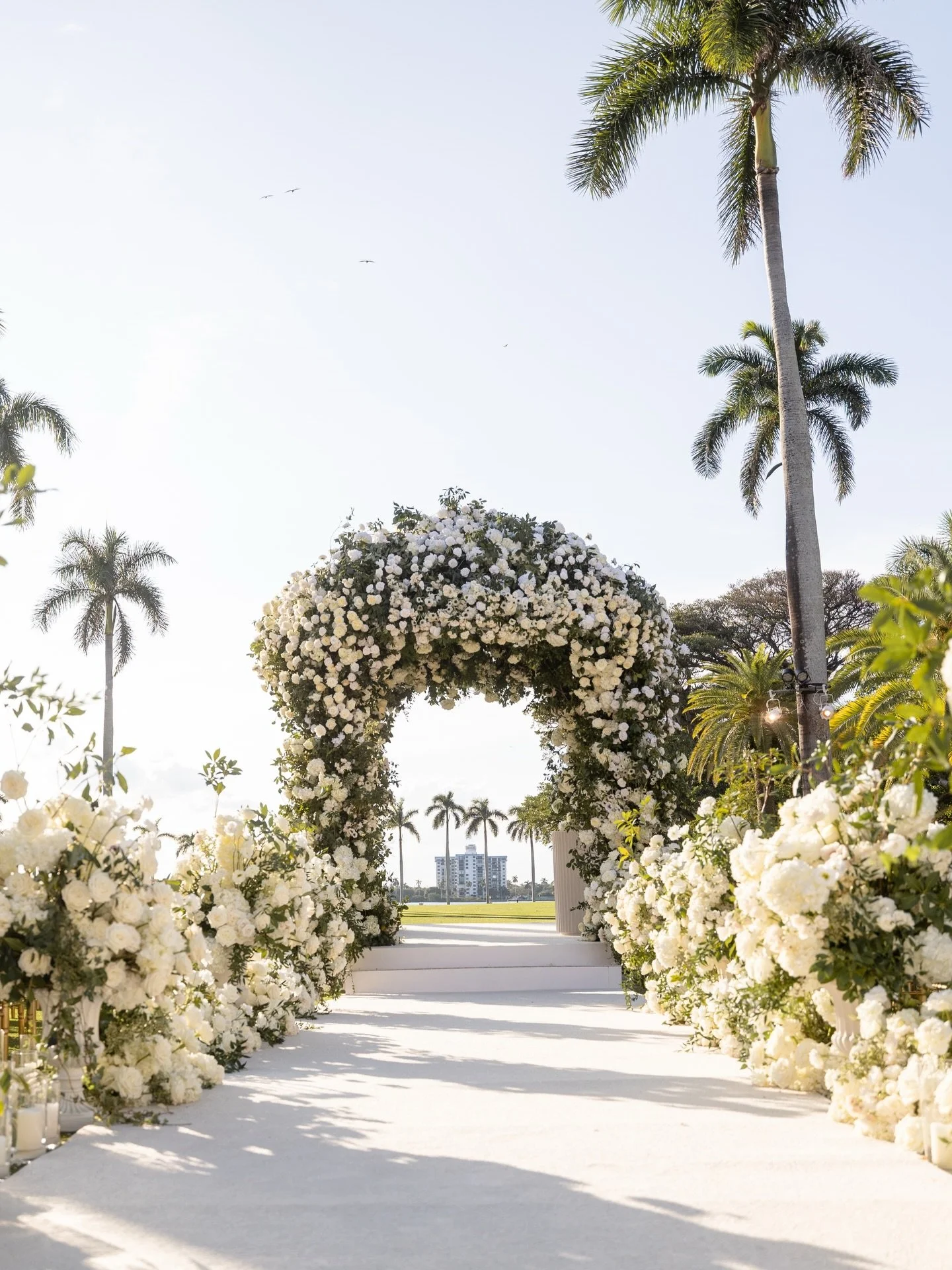 Halle and Dillon got to feel like the only two people on earth, while surrounded by a circular ceremony full of everyone they love. White garden roses, hydrangea, and ranunculus built into an arch against a Palm Beach skyline, two walls of white bloo