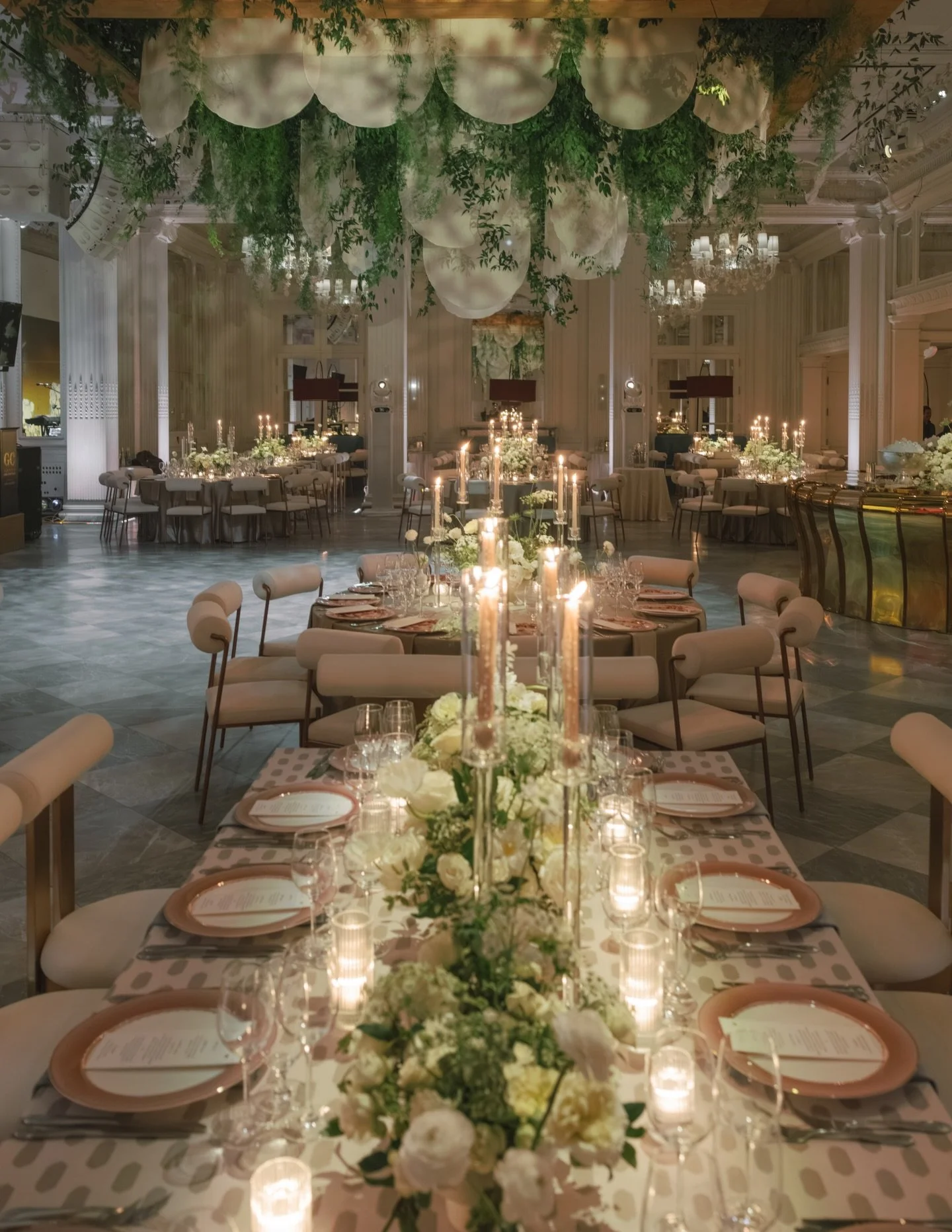 A scalloped organza ceiling sets the tone, soft yet architectural, with greenery cascading through every fold. Burgundy velvet lamps introduce an unexpected, moody contrast, while florals feel layered, slightly vintage, and garden driven. The band ba