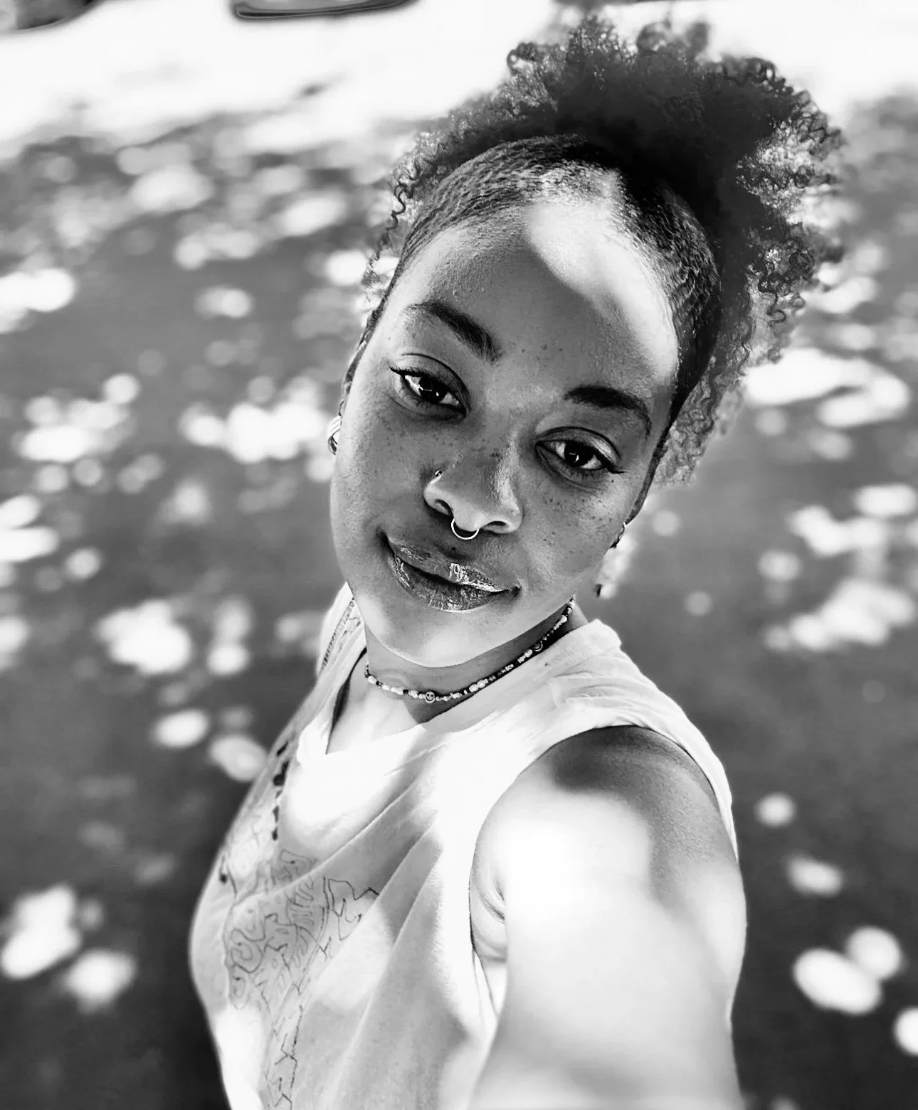 A woman taking a selfie at the beach, with water and floating shells in the background, in black and white.