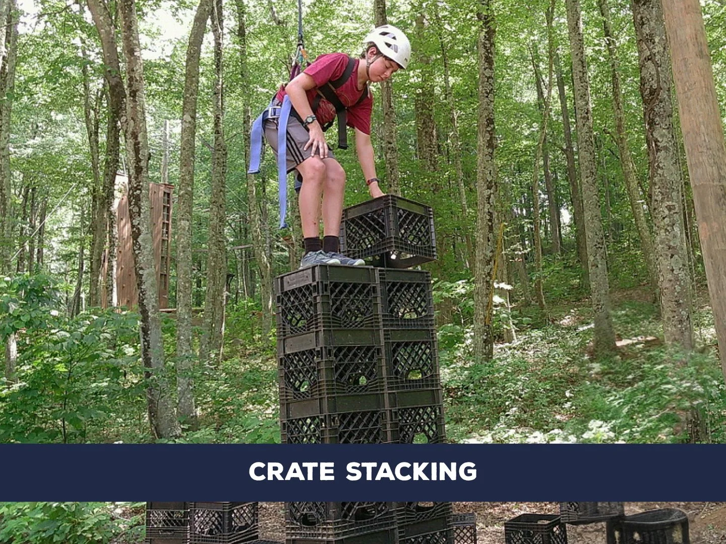 Stack and climb milk crates while harnessed, aiming to stand as high as possible before the tower tips.