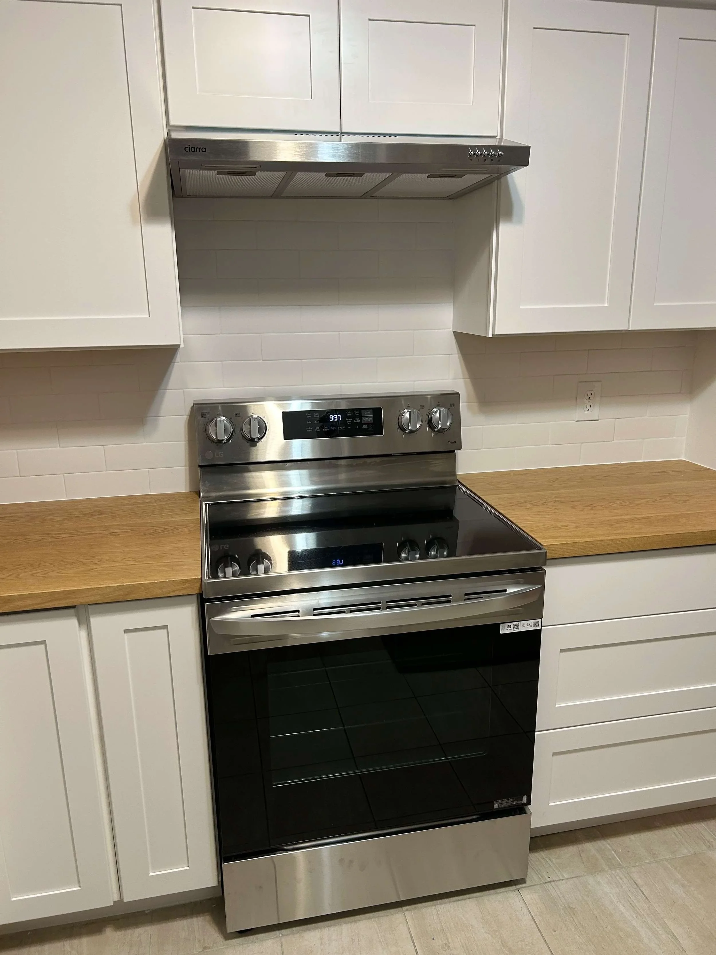 Stainless steel LG electric range oven in a modern kitchen with white cabinets and a wood countertop.