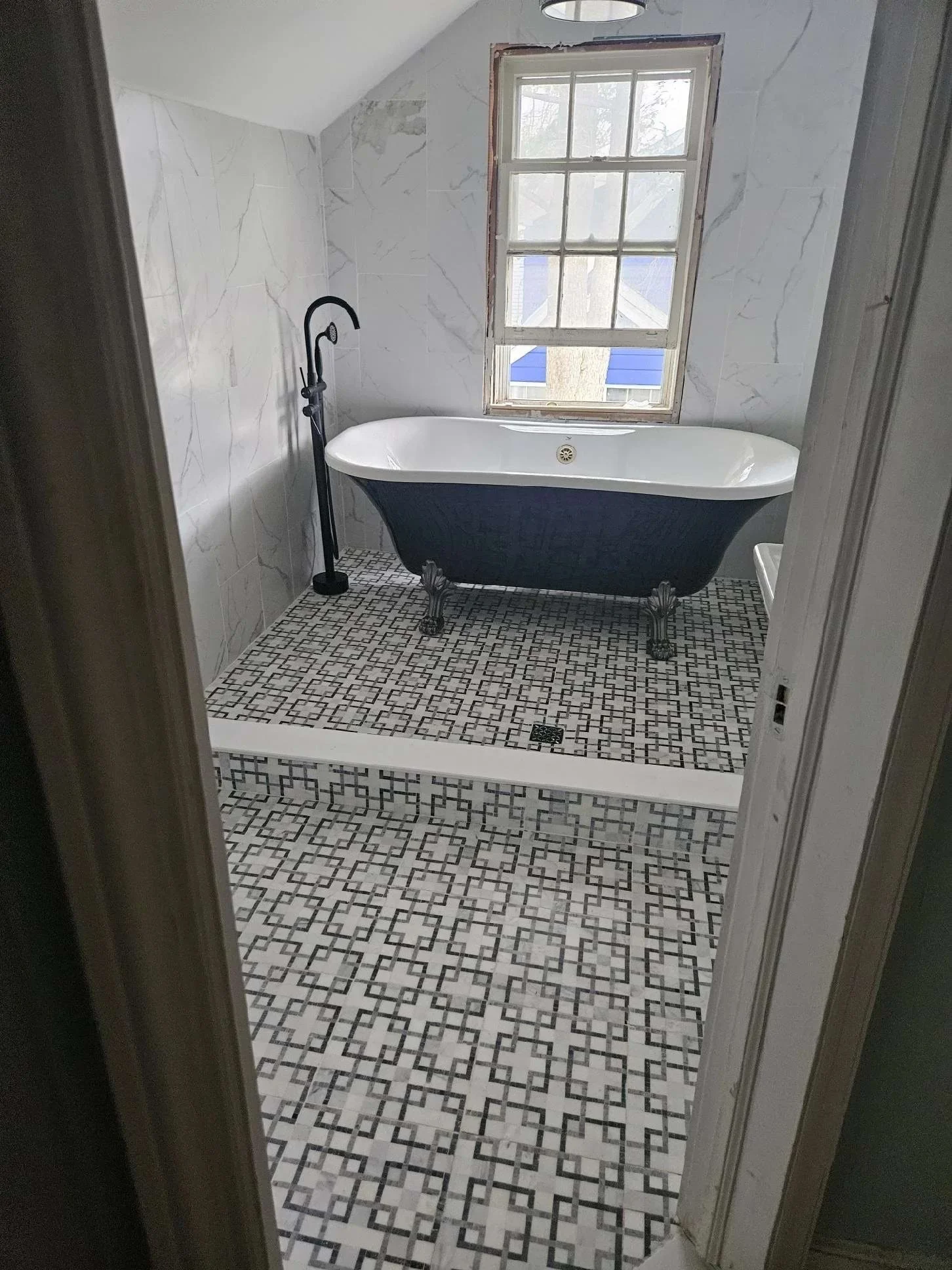 Bathroom with clawfoot tub, black fixtures, patterned floor, marble walls, small window, ceiling light, and small sink.