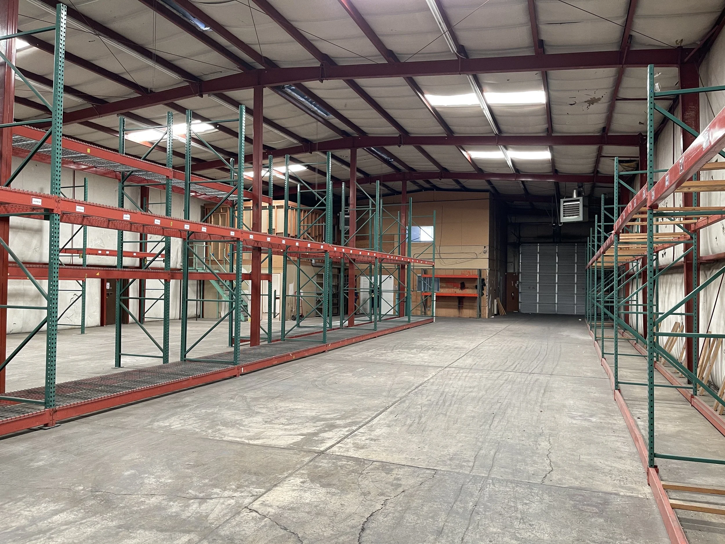Empty warehouse with metal shelving units on both sides and a large door at the back.