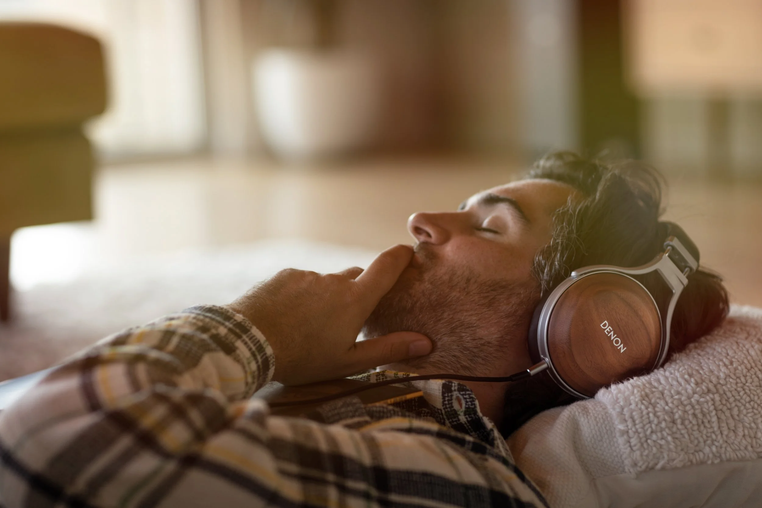 A man lying down with eyes closed, wearing headphones, with another person's hand touching his lips.